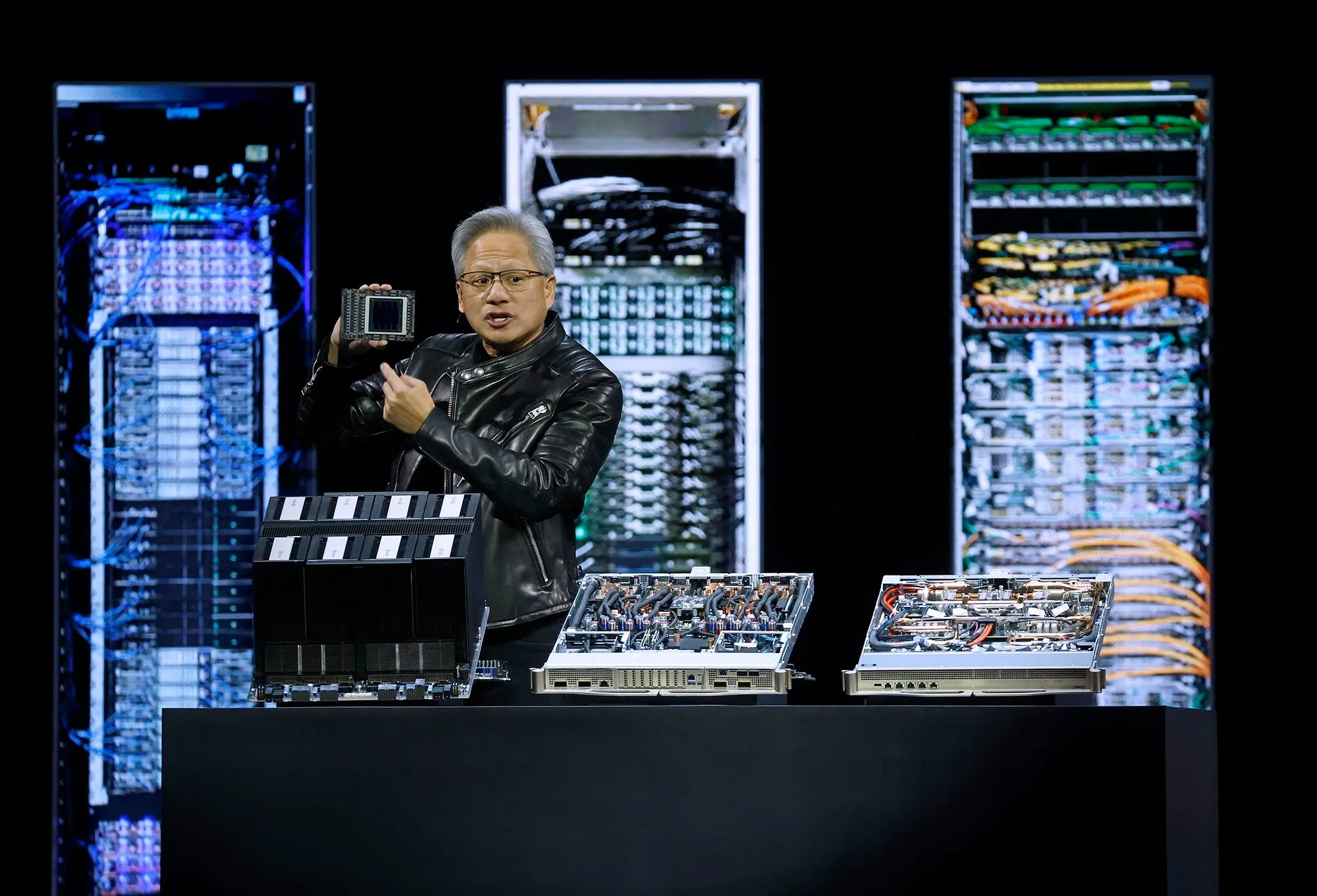 رئيس شركة Nvidia يعرض رقاقة RTX Spark الجديدة للحواسيب المحمولة، مع خلفية من الخوادم، في مؤتمر تقني حول الذكاء الاصطناعي.