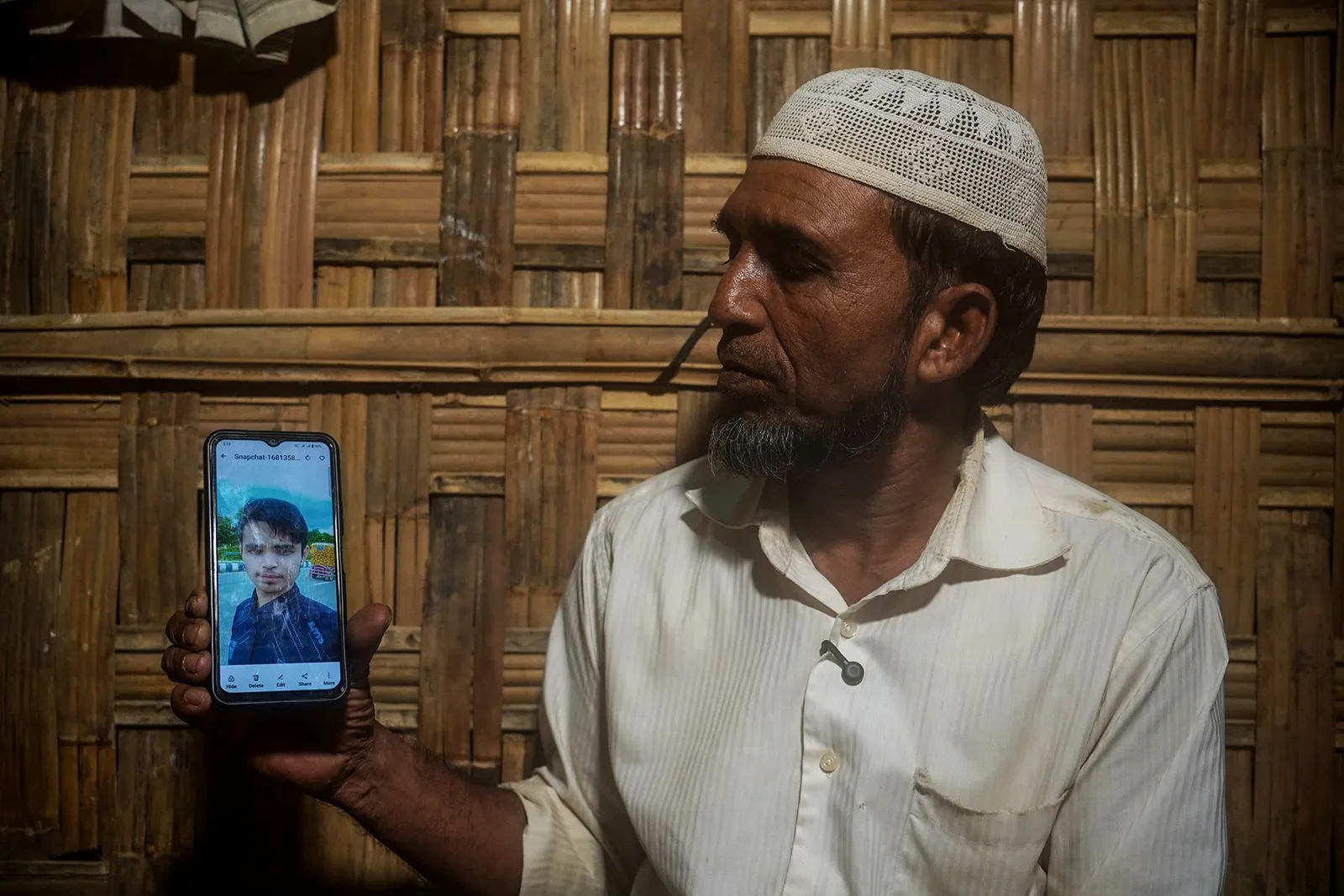 رجل روهينغي في مخيم Cox's Bazar يعرض صورة ابنه المختطف على هاتفه، معبرًا عن ألم فقدانه وظروف اللاجئين الصعبة.