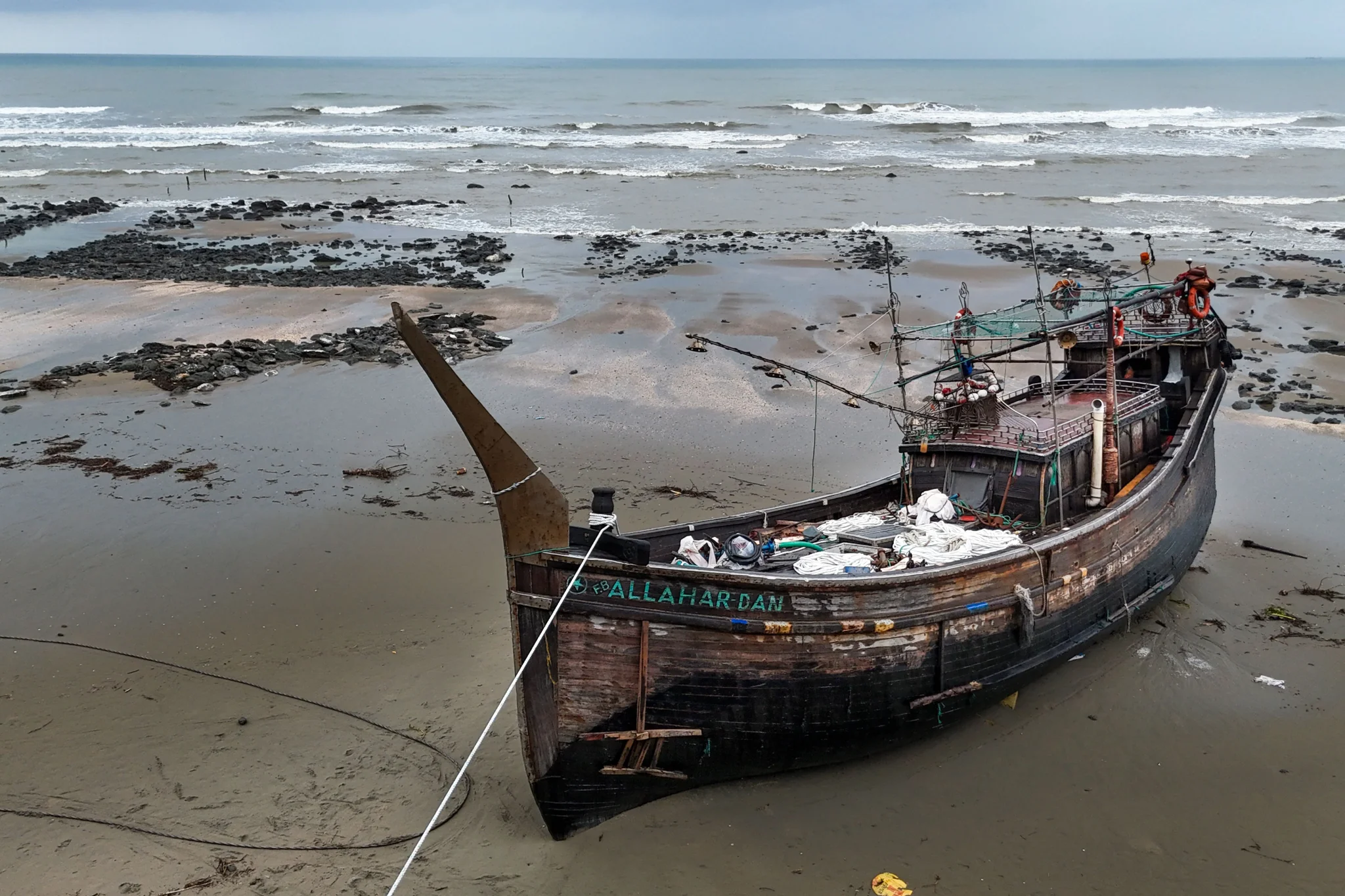 سفينة خشبية مهجورة على شاطئ طيني قرب مخيم Cox's Bazar، تعكس مخاطر الرحلات البحرية للاجئين الروهينغا في 2024.