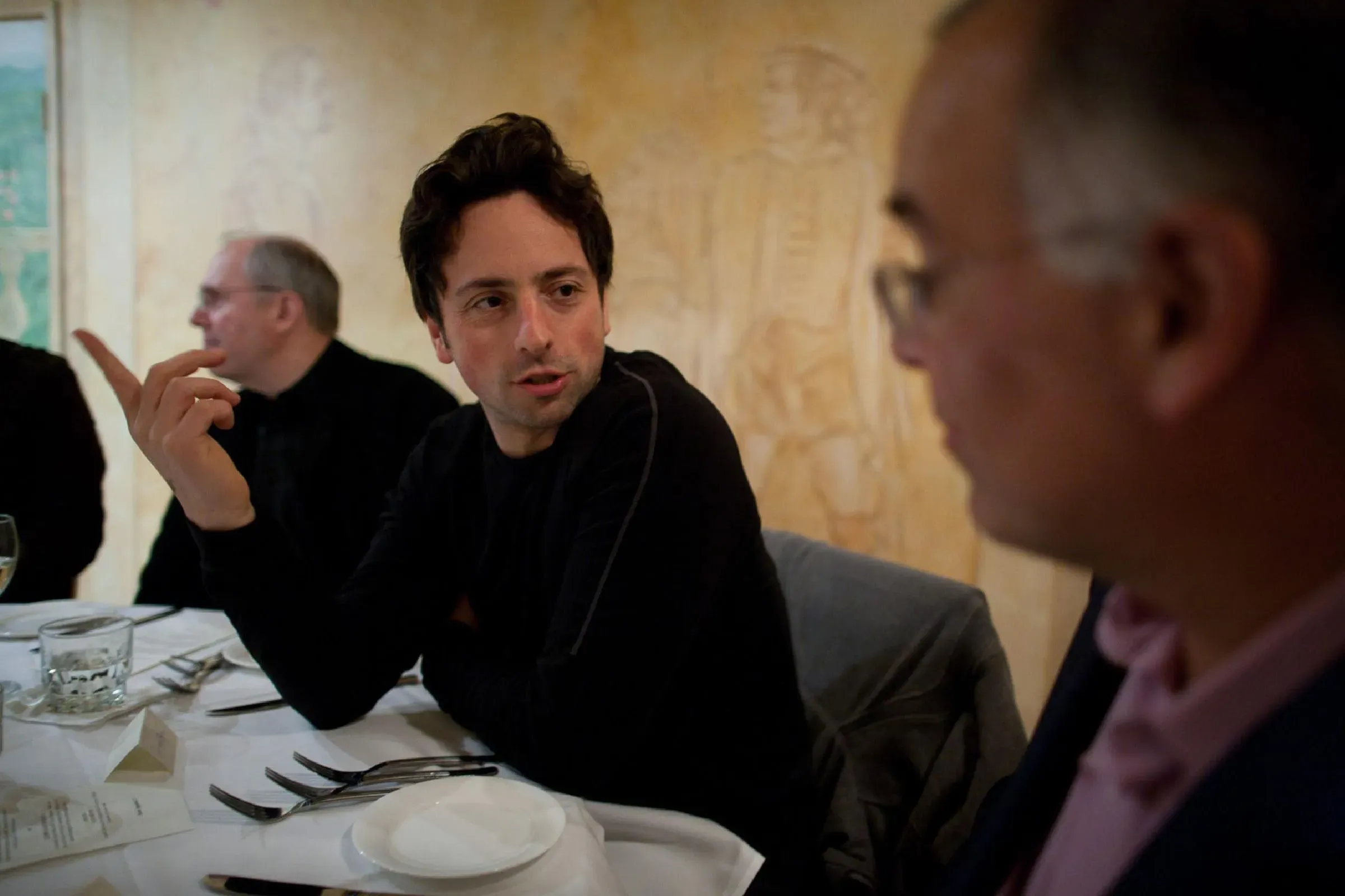 تظهر الصورة شخصين يتحدثان خلال عشاء، مع وجود طاولة مزينة بأطباق وأكواب. تعكس الأجواء تفاعلاً غير رسمي.