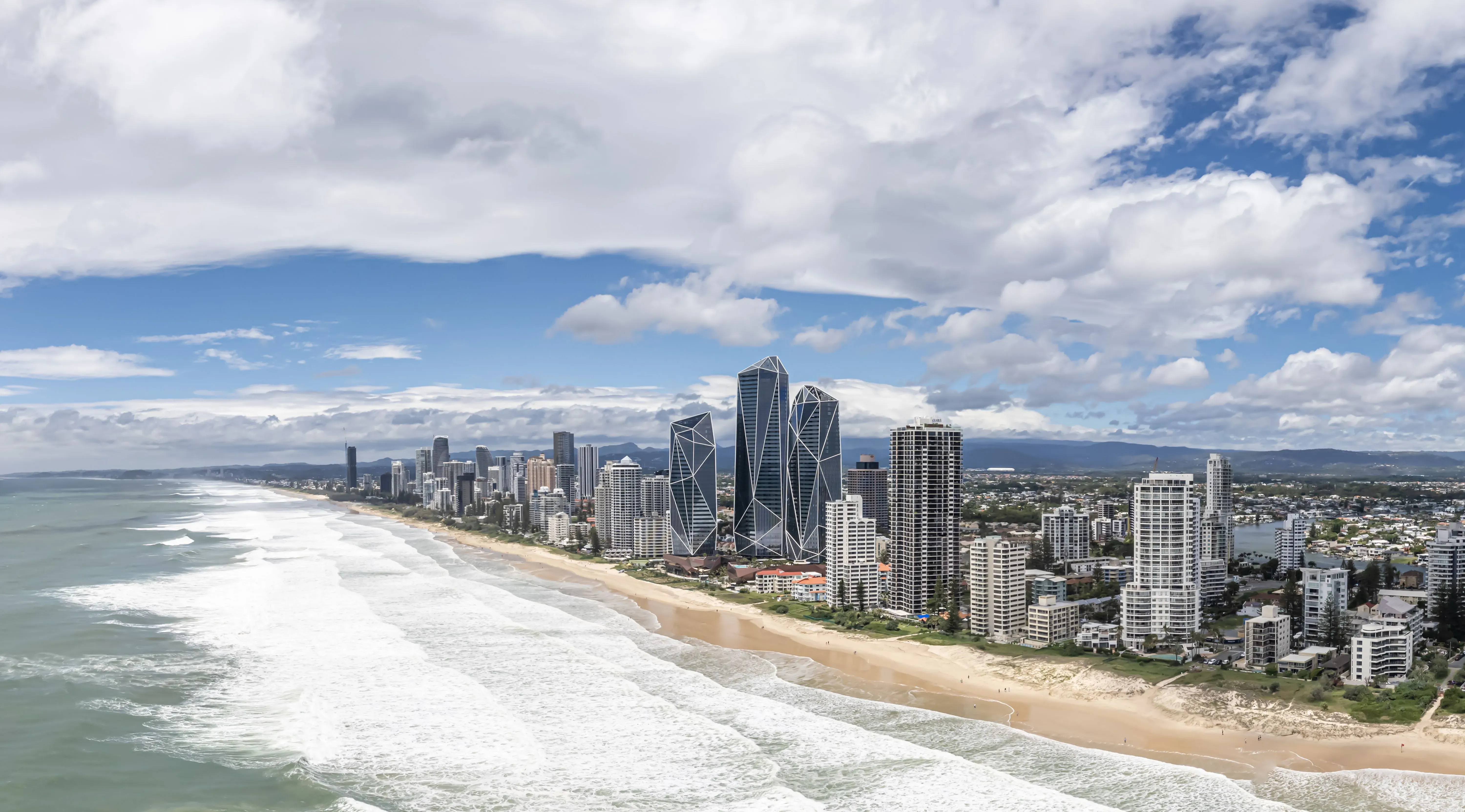 صورة لواجهة ساحل جولد كوست، تُظهر الأبنية الحديثة والشاطئ، مع أمواج البحر تحت سماء زرقاء ملبدة بالغيوم، تعكس خطط تطوير برج ترامب المقترح.