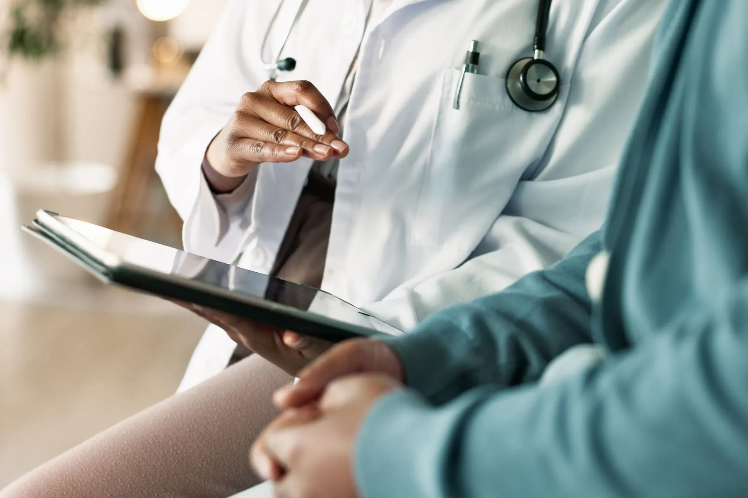 طبيب يرتدي معطفًا أبيضًا ويستخدم جهاز لوحي لمناقشة المعلومات مع مريض، مما يعكس أهمية الرعاية الصحية في ظل نقص الأطباء.