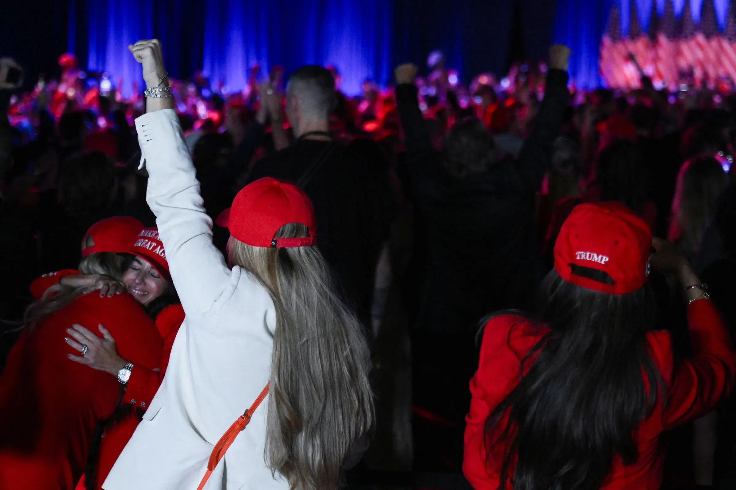 حضور حشد من مؤيدي ترامب في تجمع سياسي، يرتدون قبعات حمراء ويرفعون أيديهم تعبيرًا عن الحماس والدعم.