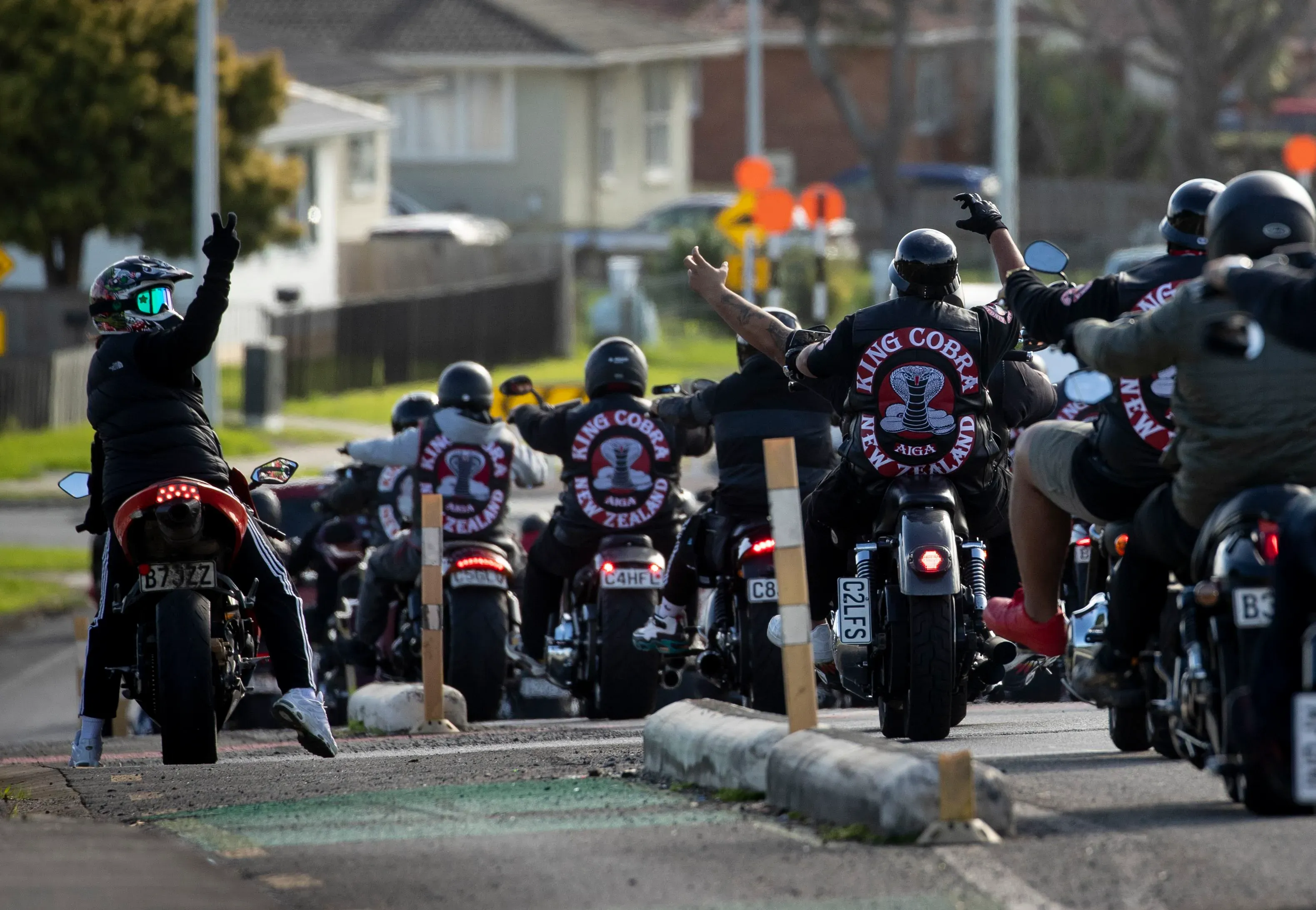 مجموعة من راكبي الدراجات النارية يرتدون سترات تحمل شعار "كينغ كوبرا" في نيوزيلندا، يرفعون أيديهم في إشارة.