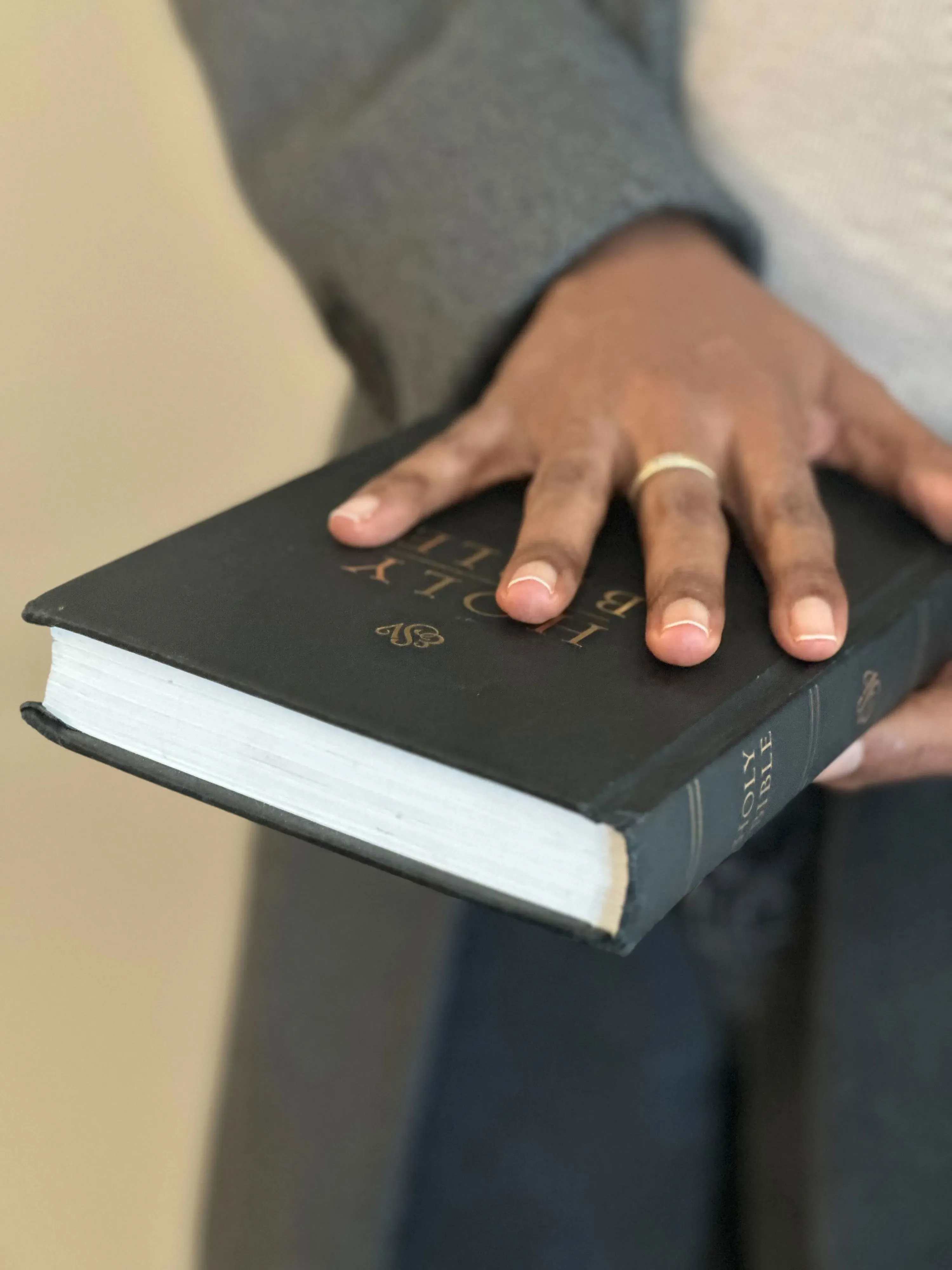 يد تحمل كتابًا أسود بعنوان "الكتاب المقدس"، مما يعكس أهمية الدين في حياة الأفراد، خاصة في سياق التحديات التي يواجهها المهاجرون.