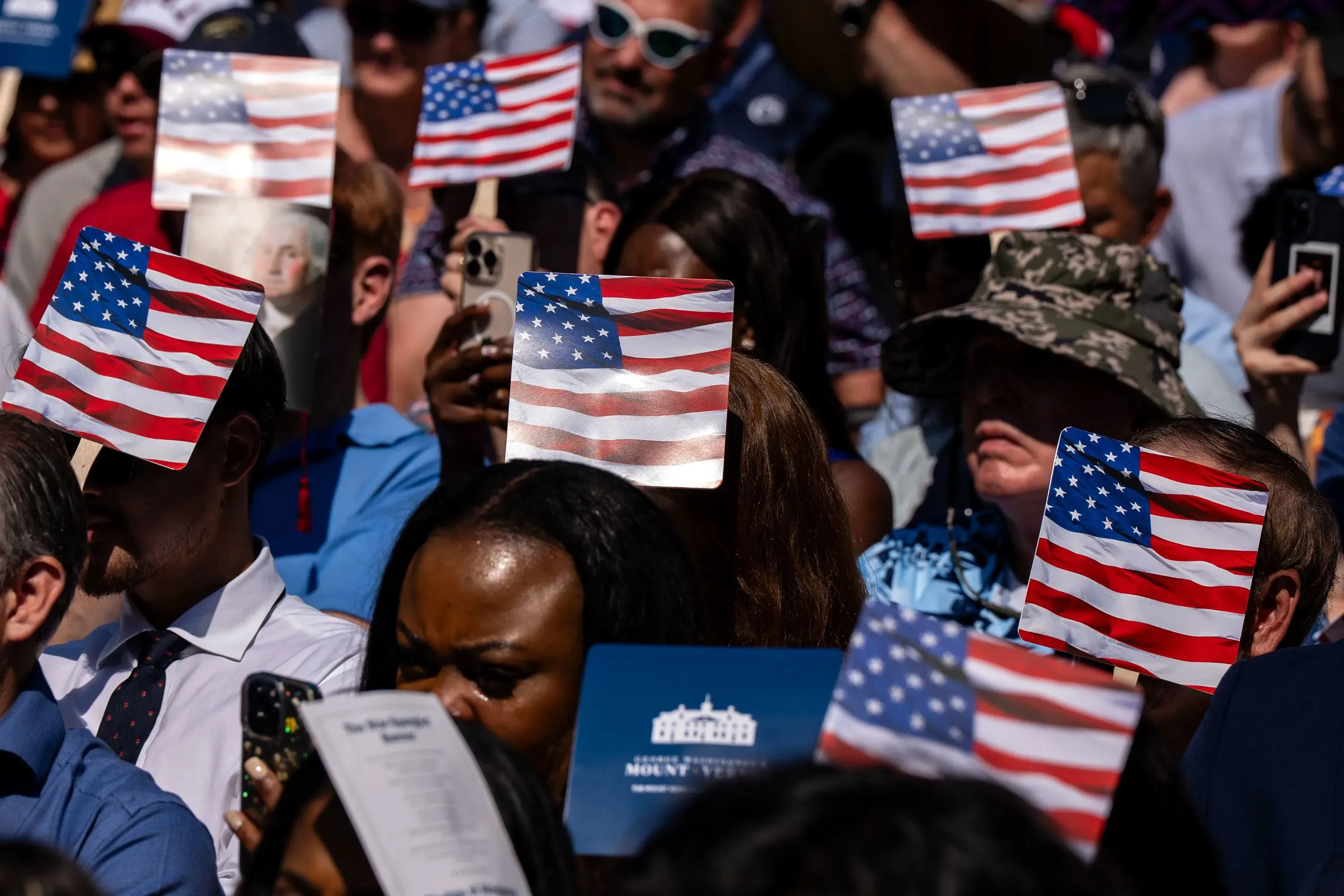 حضور حشد من الناس يحملون أعلام الولايات المتحدة خلال حدث رسمي، مما يعكس مشاعر الفخر والانتماء.