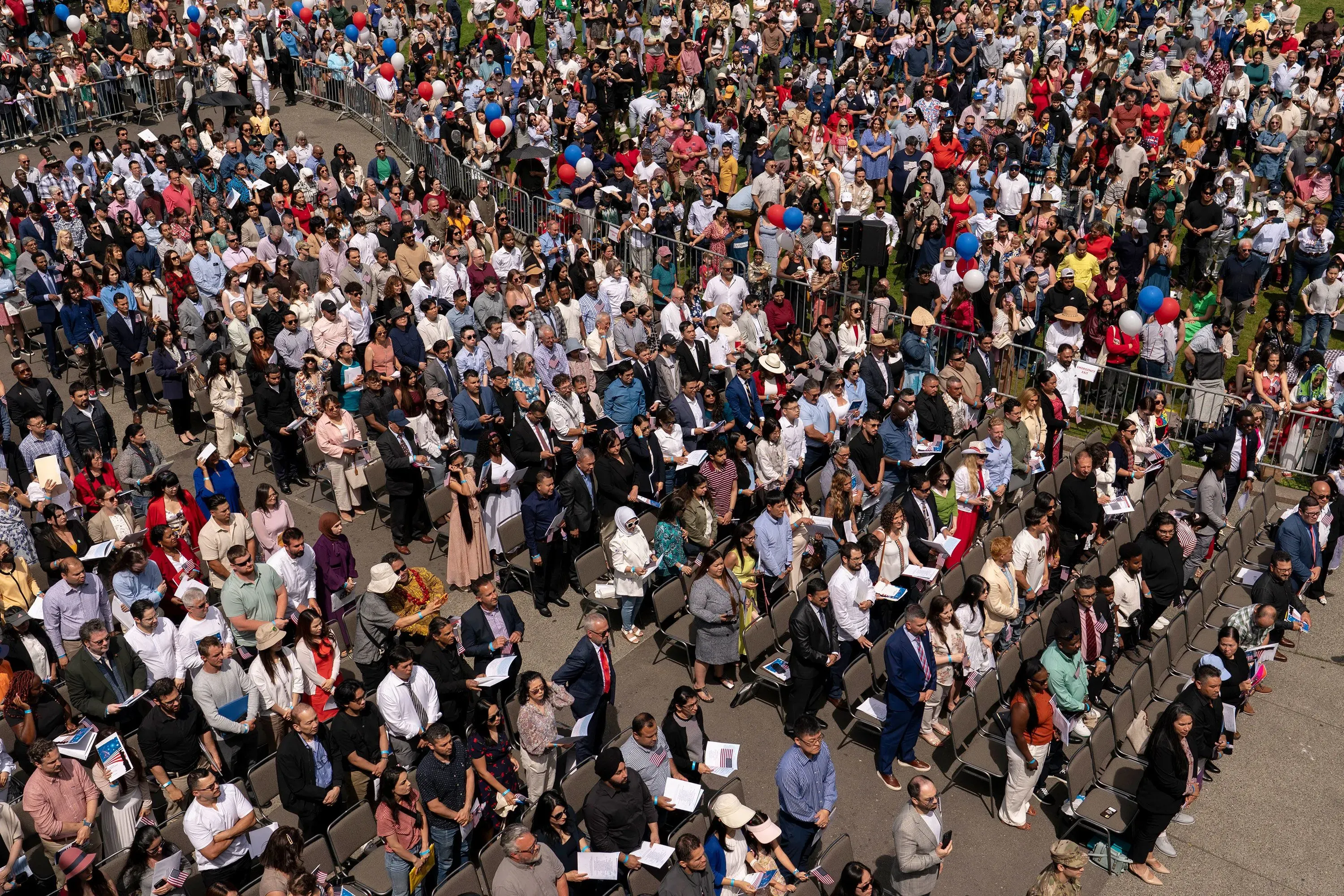 حشد كبير من المتقدمين للجنسية الأمريكية في مراسم أداء القسم، مع وجود لافتات وأعلام، تعبيراً عن الأمل والتحديات في الهجرة.