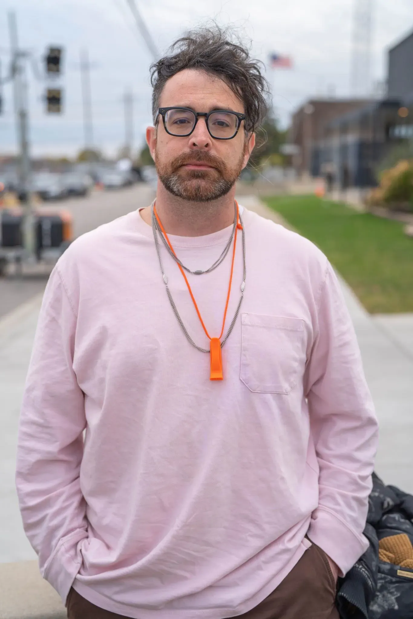 رجل يرتدي قميصًا ورديًا مع قلادة ملونة، يقف في منطقة خارج منشأة إنفاذ قوانين الهجرة في شيكاغو، وسط أجواء احتجاجات متزايدة.