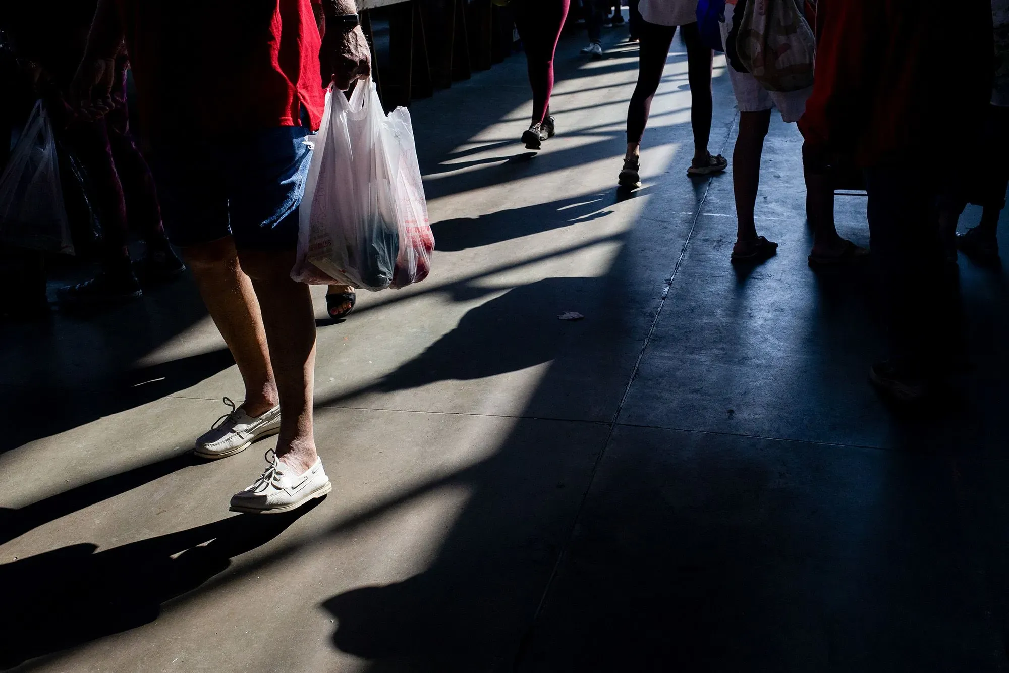 أشخاص يتسوقون في سوق مزدحم، يحملون أكياسًا بلاستيكية، مما يعكس التحديات الاقتصادية التي تواجه الأسر الأمريكية.