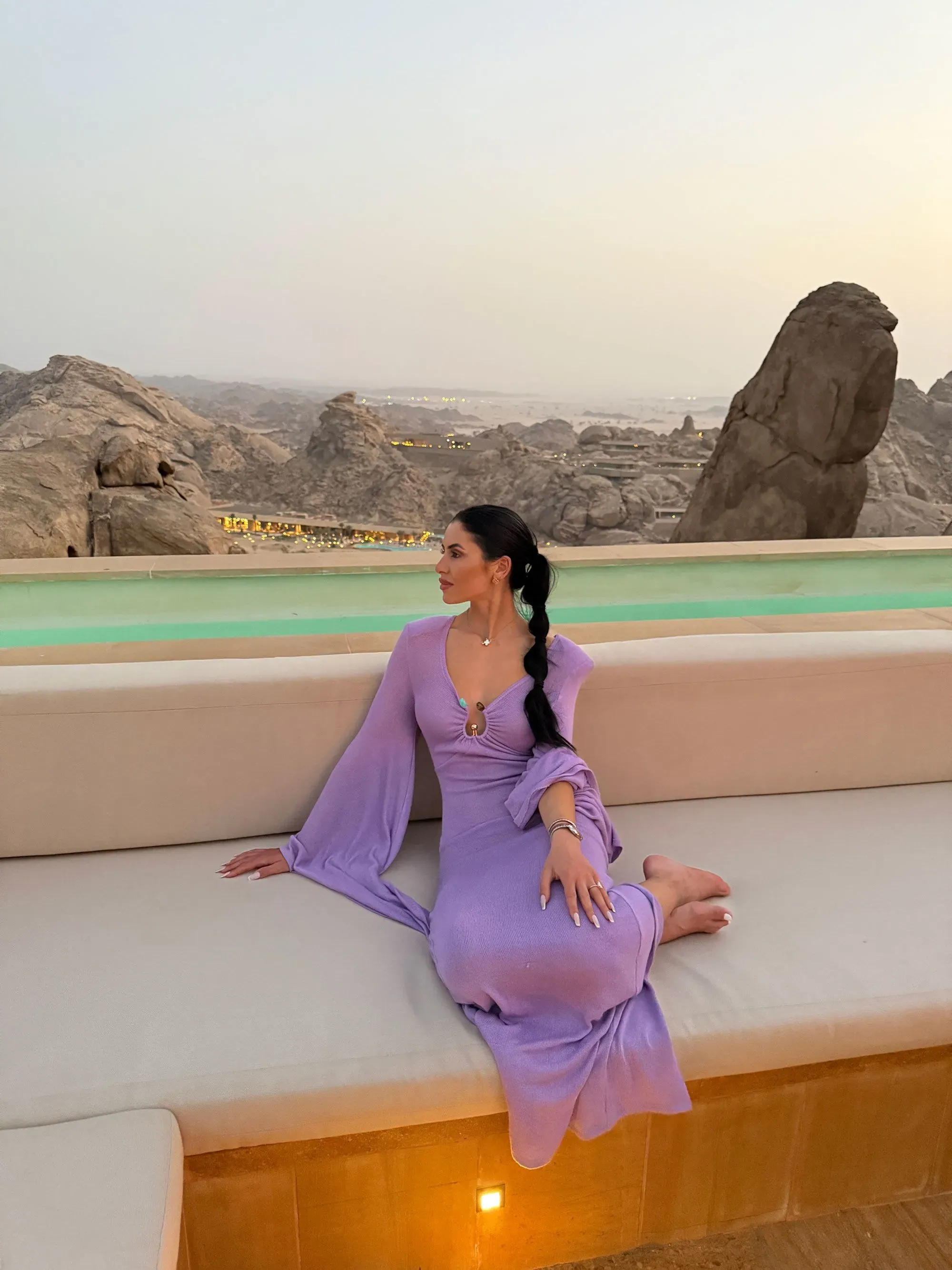 امرأة ترتدي فستاناً بنفسجياً جالساً على أريكة، مع مناظر طبيعية خلابة خلفها، تعكس اتجاهات تأجير الملابس في الاقتصاد التشاركي.