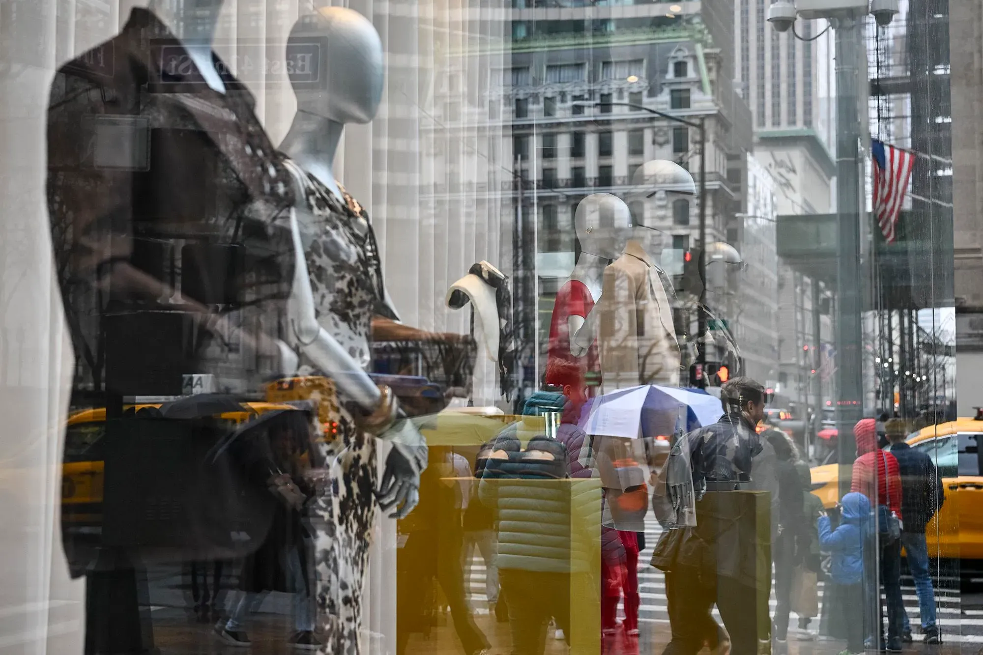 عرض لواجهة متجر في مدينة نيويورك، حيث تظهر دمى عرض ترتدي ملابس أنيقة، مع مشاة يتجولون في الشارع.