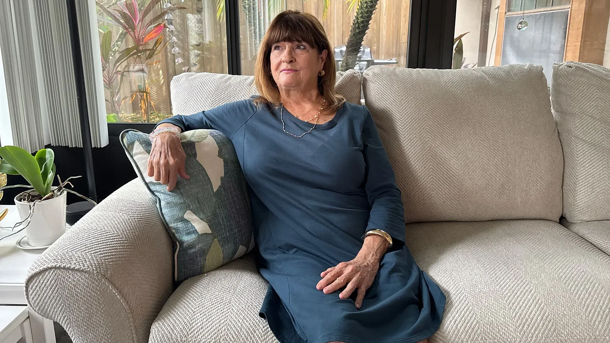 امرأة مسنّة تجلس على أريكة في غرفة مضاءة بشكل جيد، تعبر عن التأمل والهدوء، في سياق حديث عن العلاج بالسيلوسيبين.