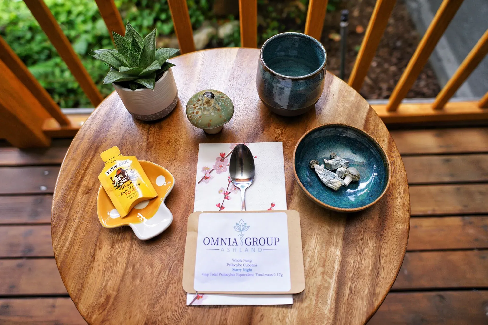 طاولة خشبية تحمل مجموعة من العناصر تشمل فطر السيلوسيبين، ملعقة، كوب، ونبات، مما يعكس تجربة علاجية جديدة في ولاية أوريغون.