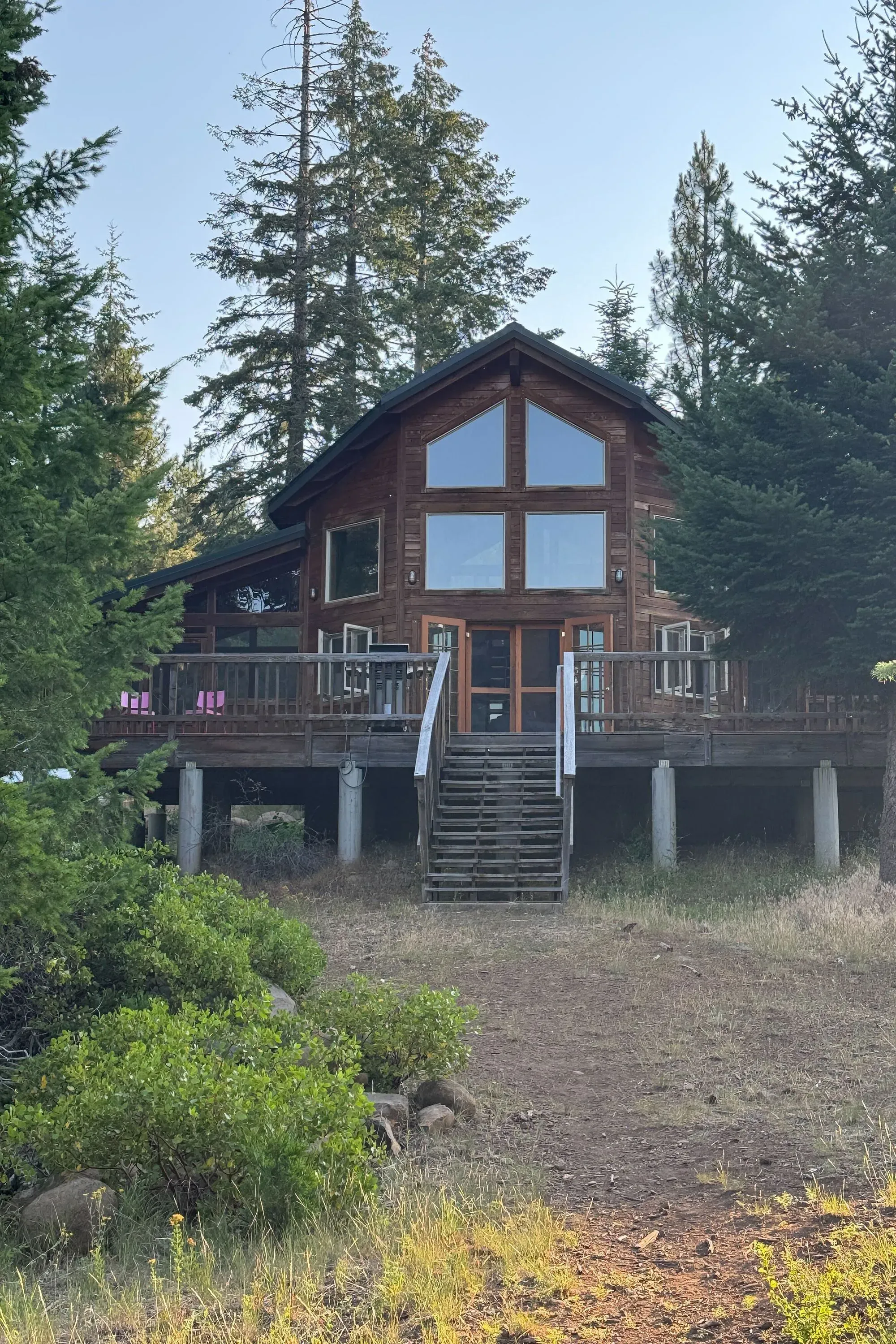 منزل خشبي محاط بالأشجار، يظهر مدخلًا مع درجات تؤدي إلى الباب الرئيسي، مما يعكس بيئة هادئة ومناسبة لجلسات العلاج بالمخدرات.