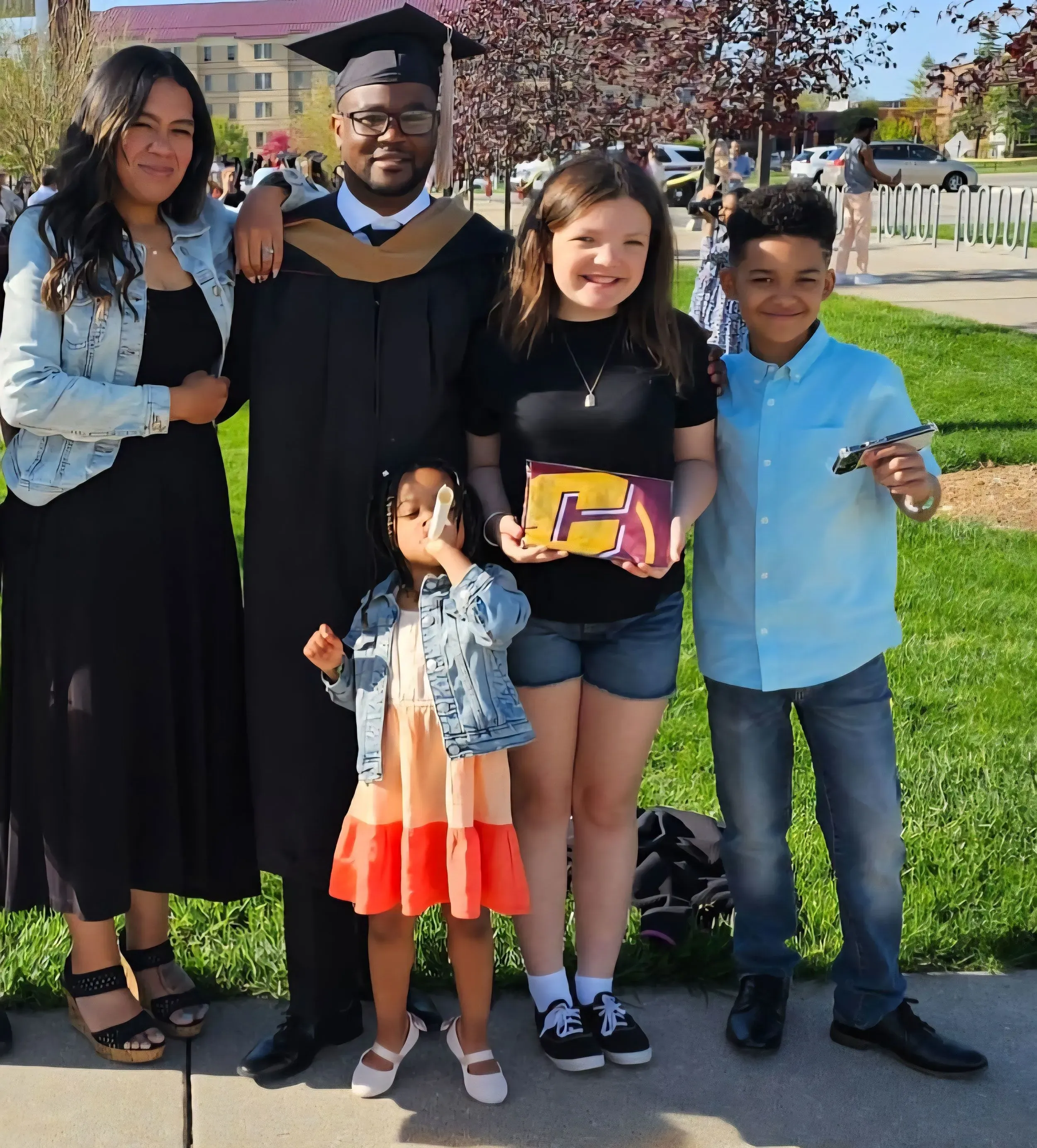 عائلة تحتفل بتخرج كانغيث، حيث يظهر مع زوجته وأطفاله الثلاثة في حديقة، مع ابتسامات تعكس الفخر والفرحة.