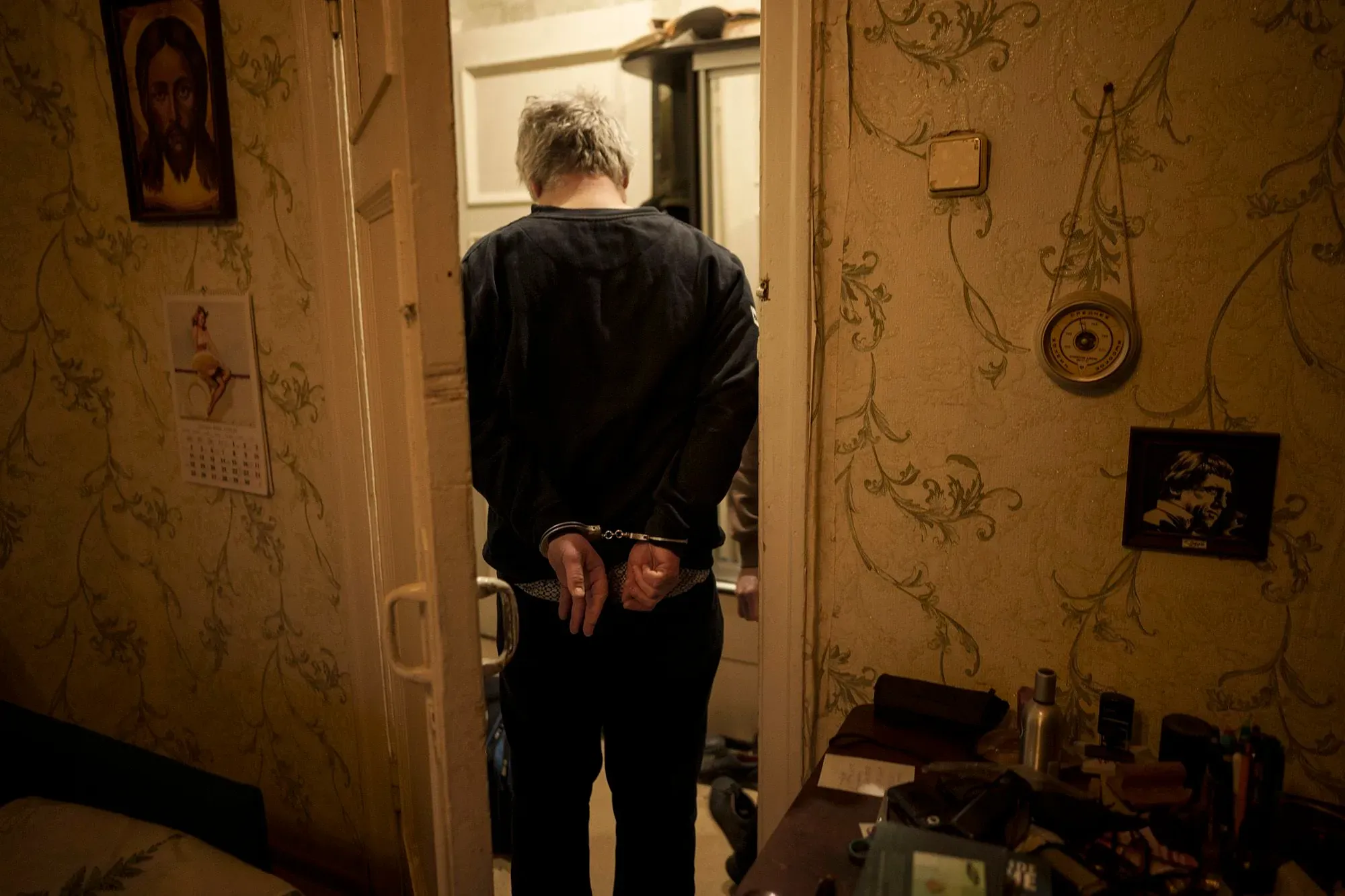 شخص مقيد اليدين بالأصفاد يقف في مدخل غرفة، مع تفاصيل جدارية وزخارف خلفه، مما يعكس سياق التحقيقات الأمنية في أوكرانيا.
