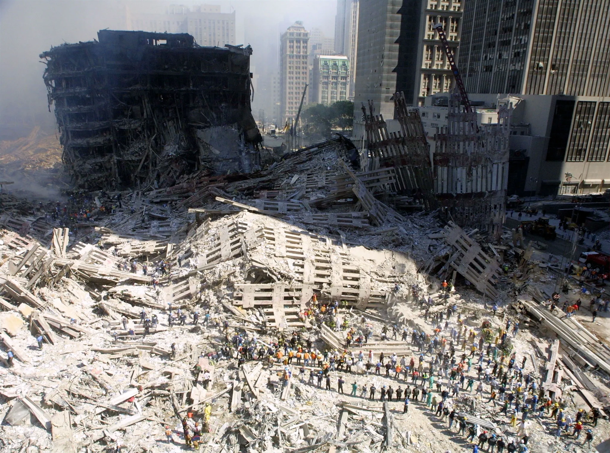 ركام موقع مركز التجارة العالمي بعد أحداث 11 سبتمبر 2001 مع فرق الإنقاذ وسط الغبار والدمار، يعكس تداعيات الكارثة الصحية والبيئية طويلة الأمد.