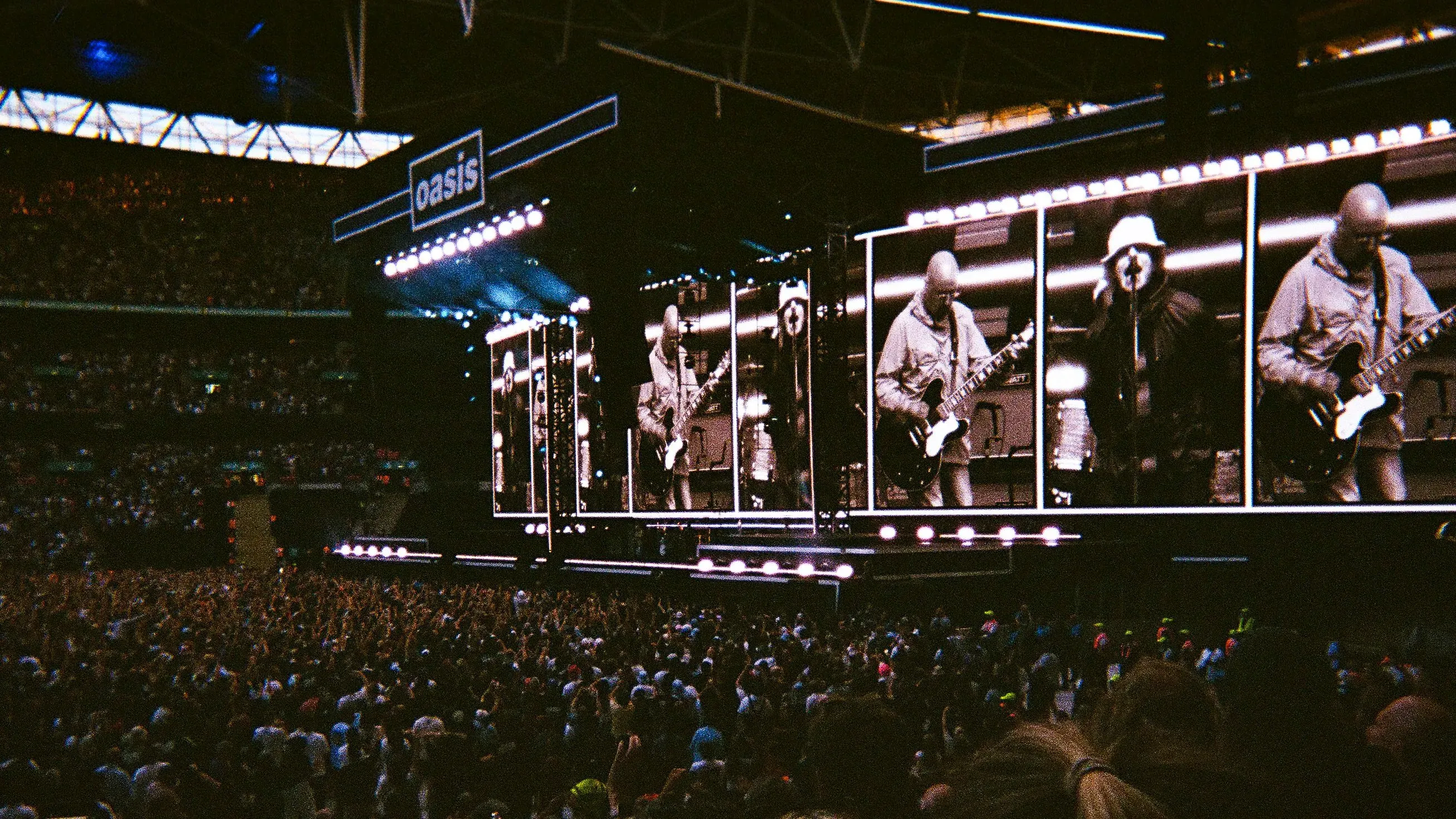 حفل فرقة Oasis في ملعب ويمبلي، حيث يتفاعل 90,000 مشجع مع الأداء، مع ظهور الأخوين غالاغر على المسرح.