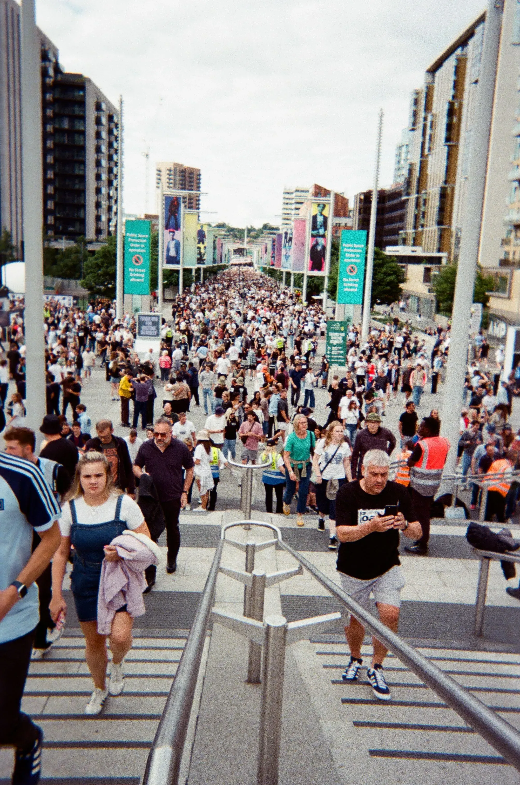 حشود كبيرة من المعجبين تتجه نحو ملعب ويمبلي، مع لافتات ترويجية لفرقة Oasis، تعكس حماس العودة في جولة لم الشمل.