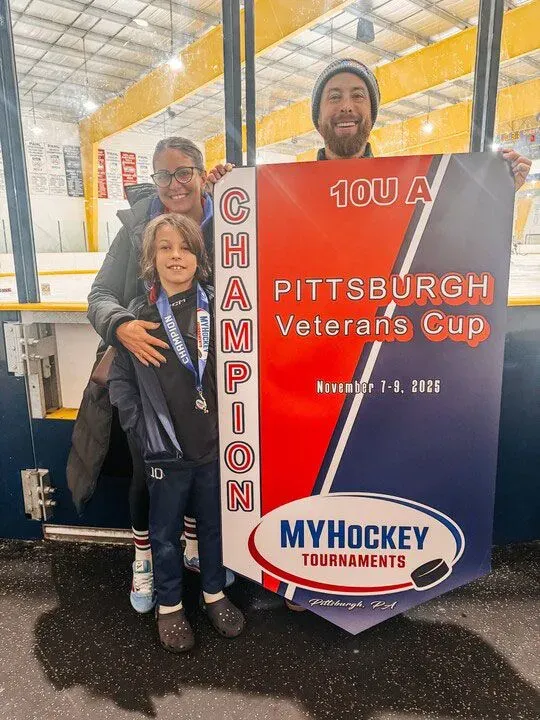 عائلة تحتفل بفوز ابنهم في بطولة هوكي، يحملون لافتة "بطل" في كأس المحاربين القدامى في بيتسبرغ، نوفمبر 2025.
