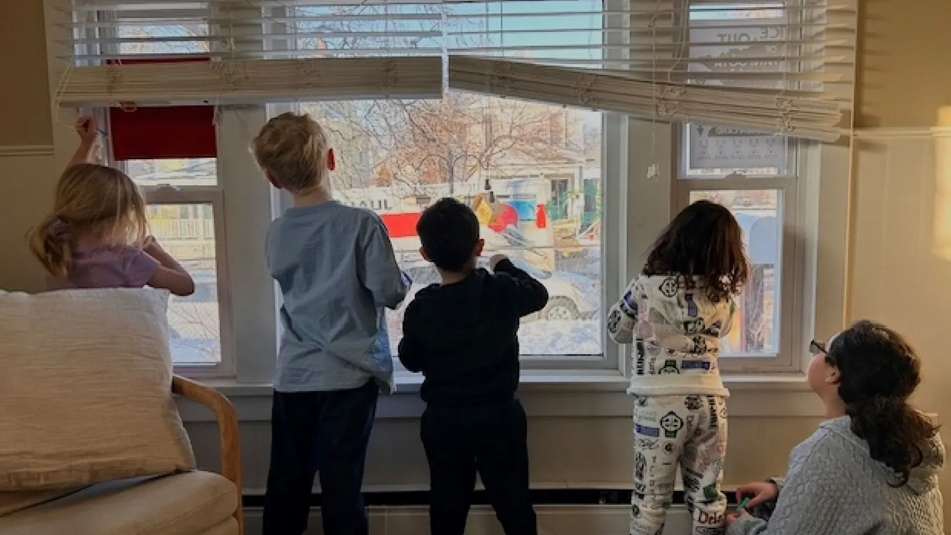 أطفال يشاهدون من نافذة منزلهم شاحنة نقل، مع تعبيرات فضولية على وجوههم، في مشهد يعكس قلق المجتمع في مينيسوتا.