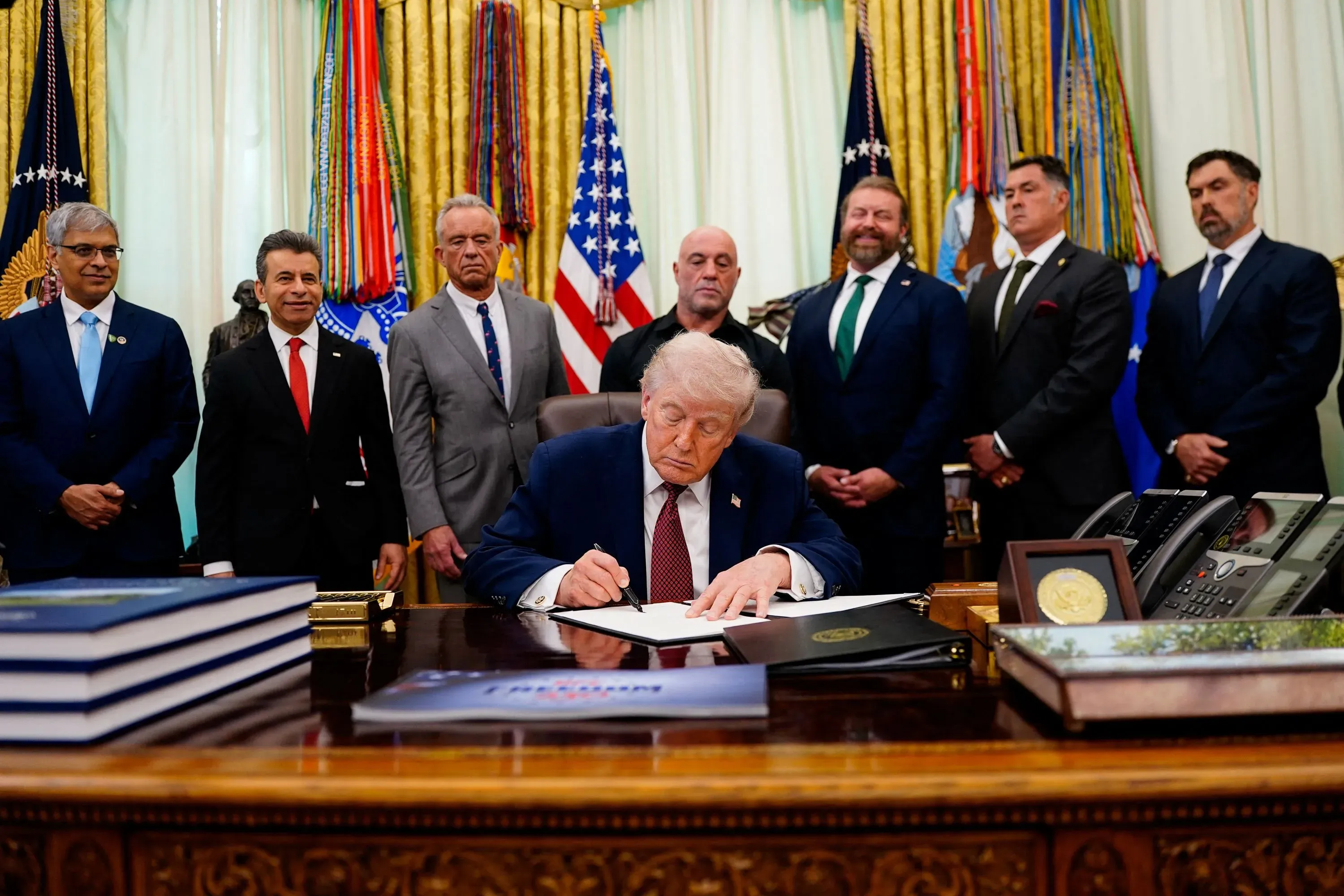 الرئيس ترامب يوقع مرسوماً تنفيذياً في المكتب البيضاوي لتعزيز الأبحاث حول العقاقير المُهلوِسة لعلاج الصحة النفسية، محاطاً بمستشارين.