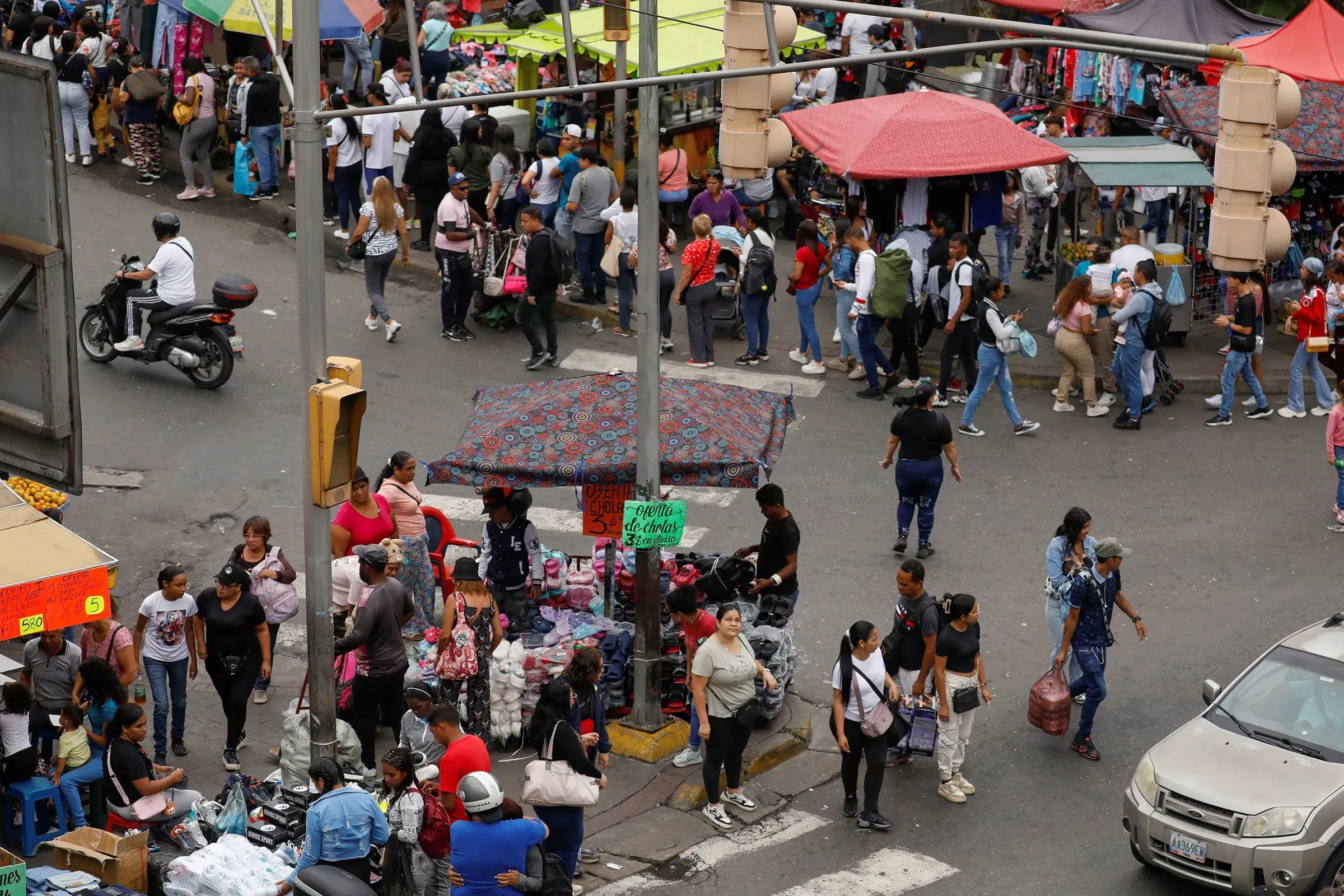 سوق مزدحم في مدينة، حيث يتجمع الناس حول أكشاك الملابس والسلع، مما يعكس حركة المهاجرين الفنزويليين.