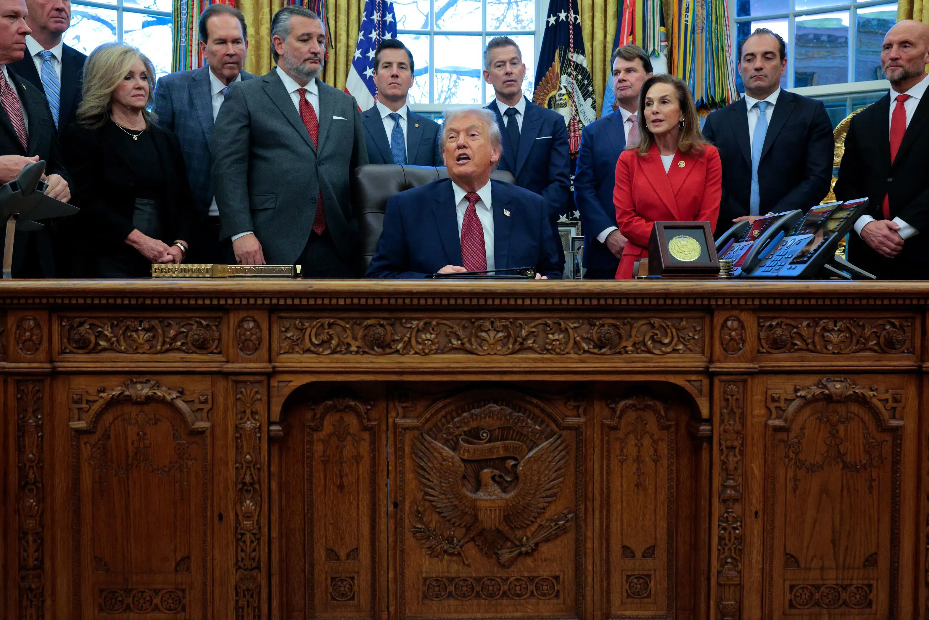 ترامب يجلس خلف مكتبه في المكتب البيضاوي، محاطًا بمساعديه، خلال اجتماع رسمي يتناول السياسة والقرارات التنفيذية.