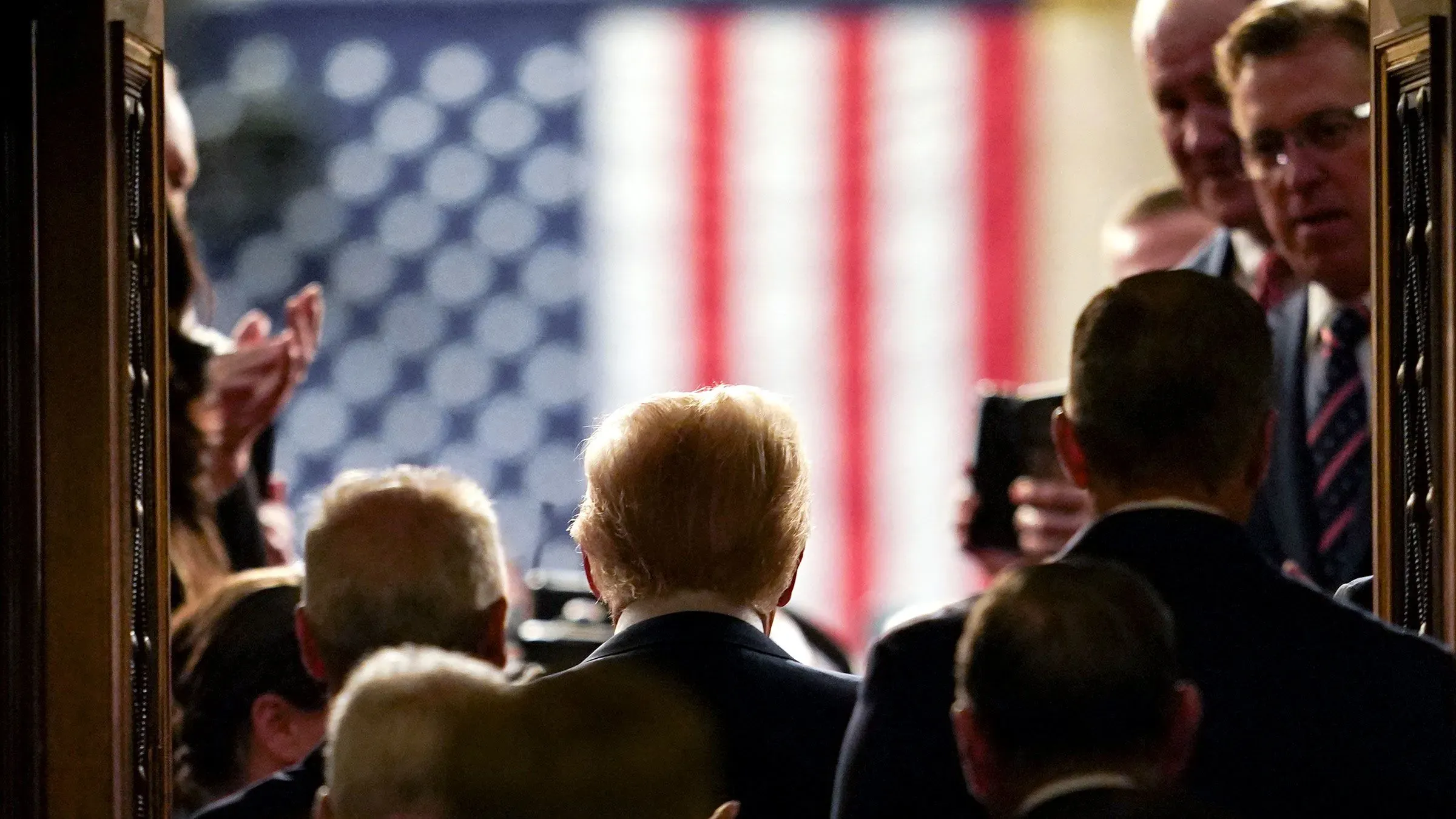 صورة لترامب من الخلف وهو يدخل قاعة الكونغرس، مع العلم الأمريكي في الخلفية، تعكس التوتر السياسي حول قضايا الإنفاق.