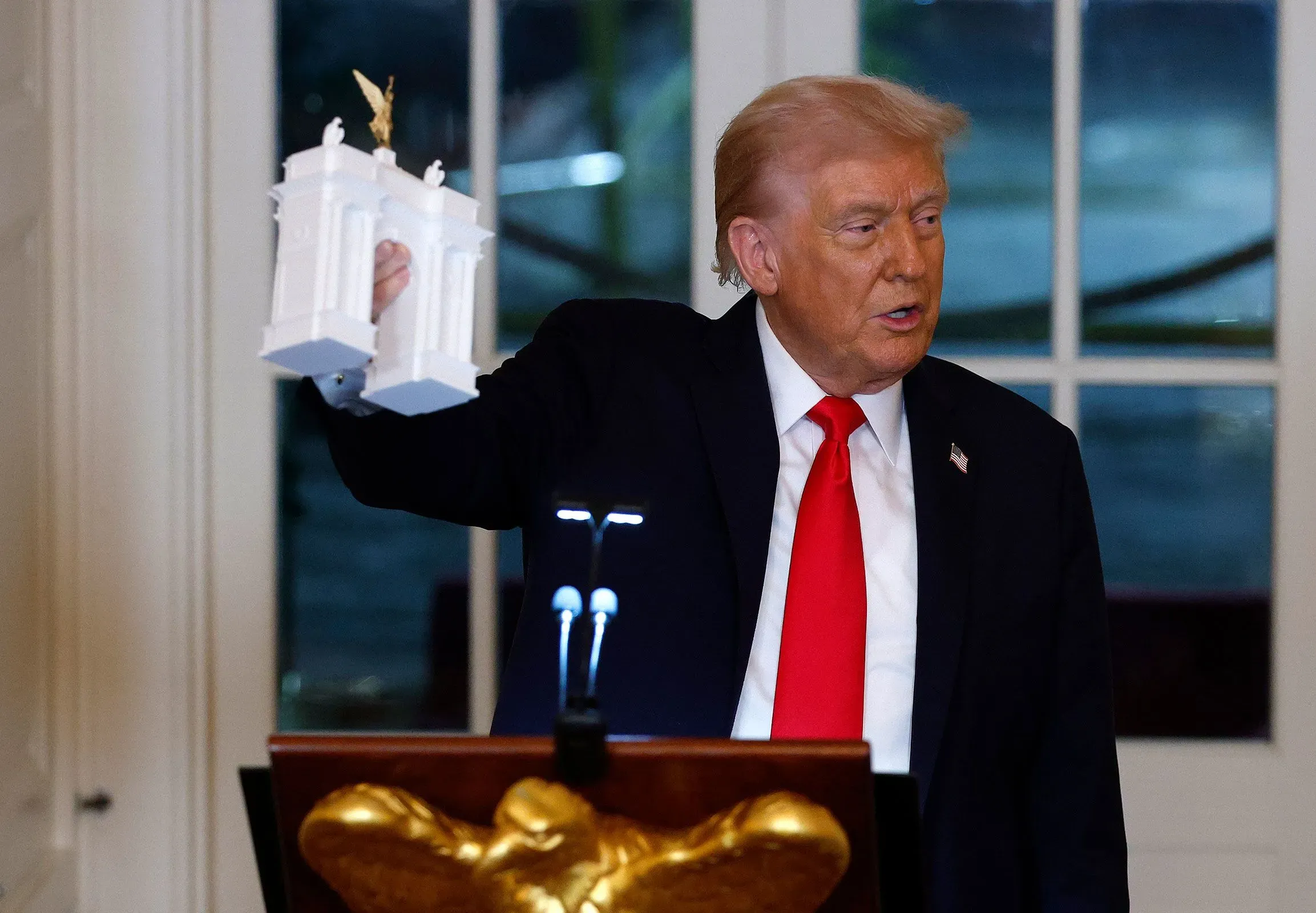 ترامب يحمل نموذجًا مصغرًا لقوس الاستقلال المقترح، الذي سيكون الأكبر في العالم، خلال مؤتمر صحفي في البيت الأبيض.