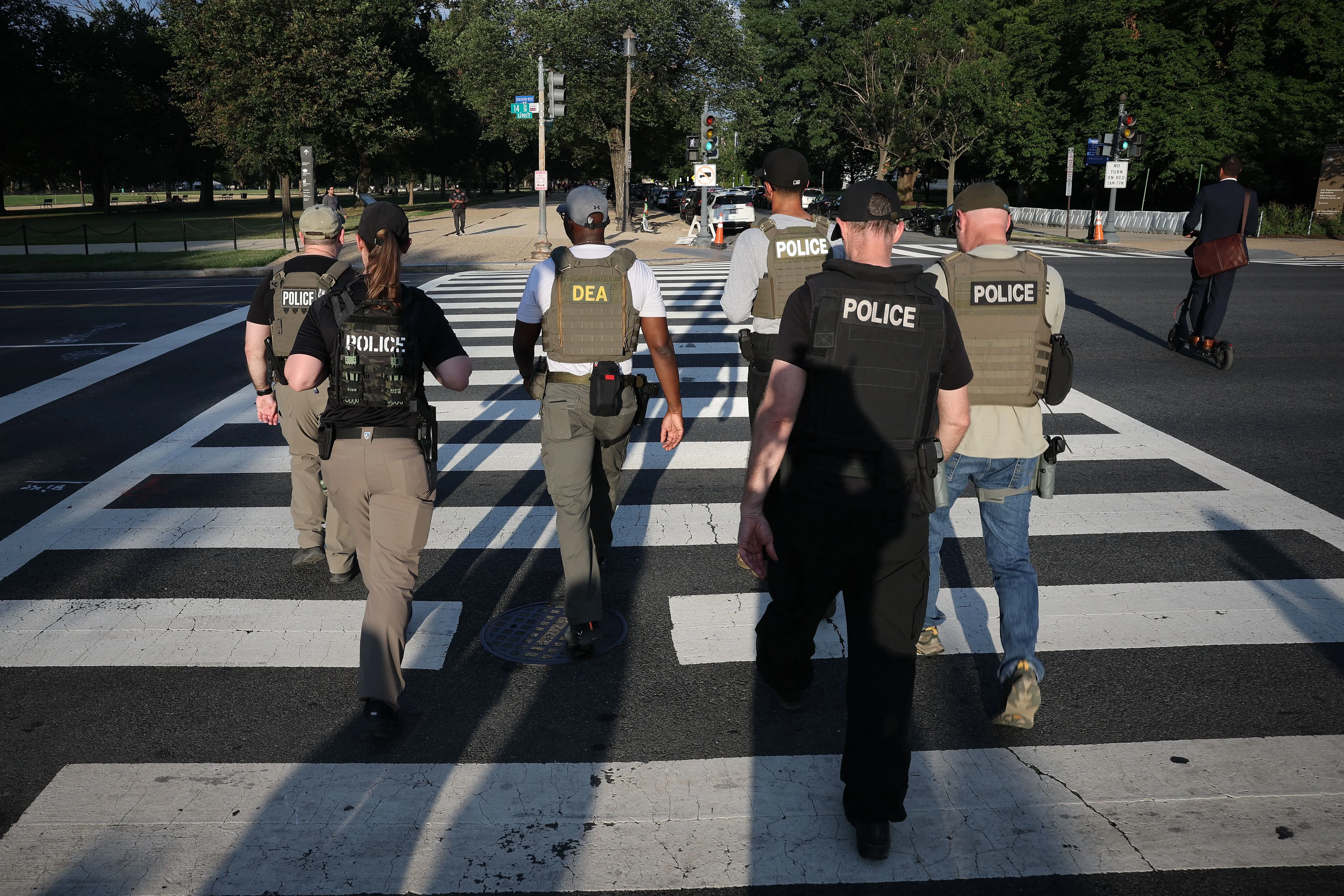 مجموعة من ضباط الشرطة ورجال مكافحة المخدرات يسيرون عبر ممر مشاة في واشنطن، مما يعكس زيادة الوجود الأمني في المدينة.
