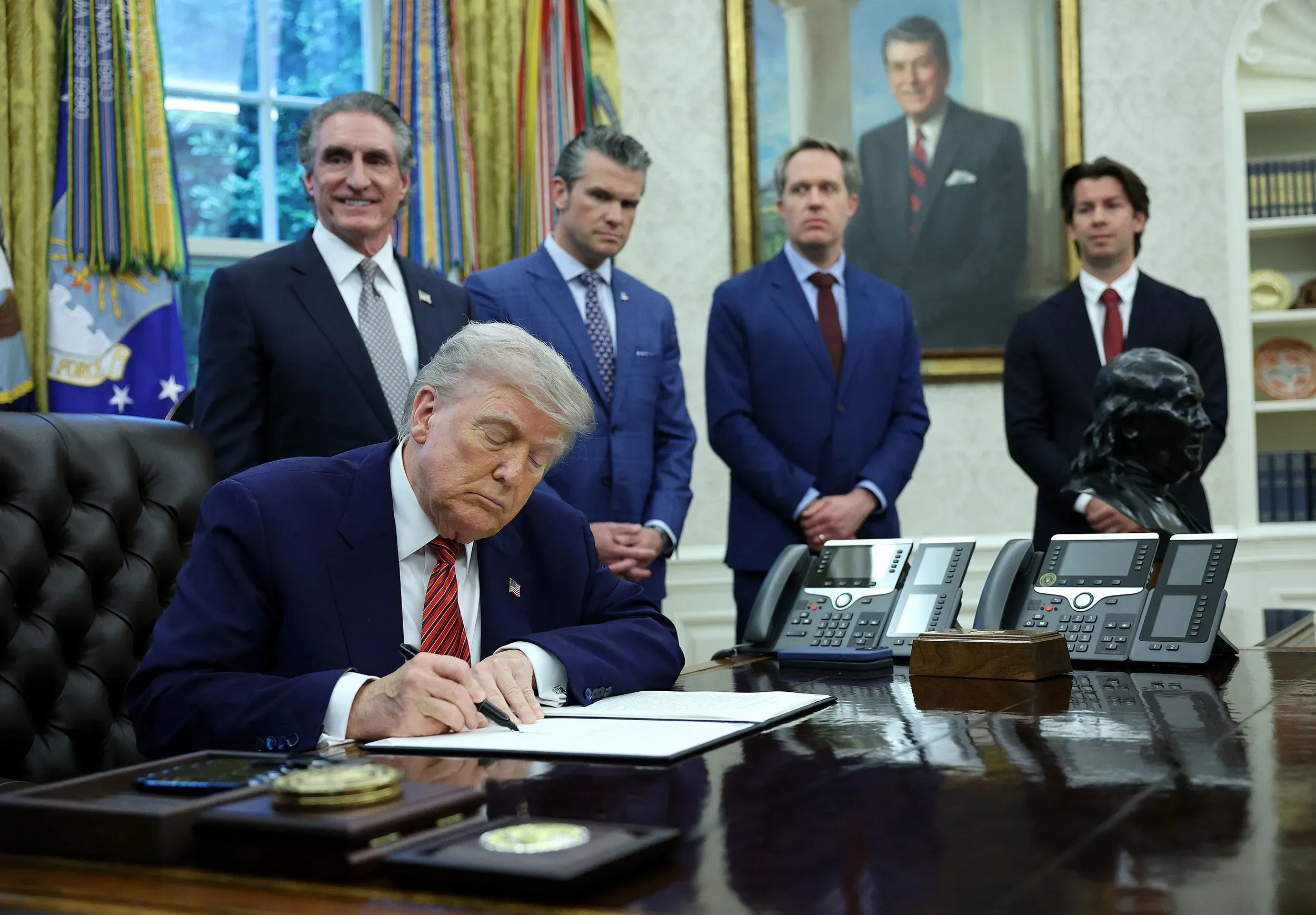 تظهر الصورة الرئيس السابق دونالد ترامب وهو يوقع وثيقة في المكتب البيضاوي، محاطًا بمجموعة من المستشارين.