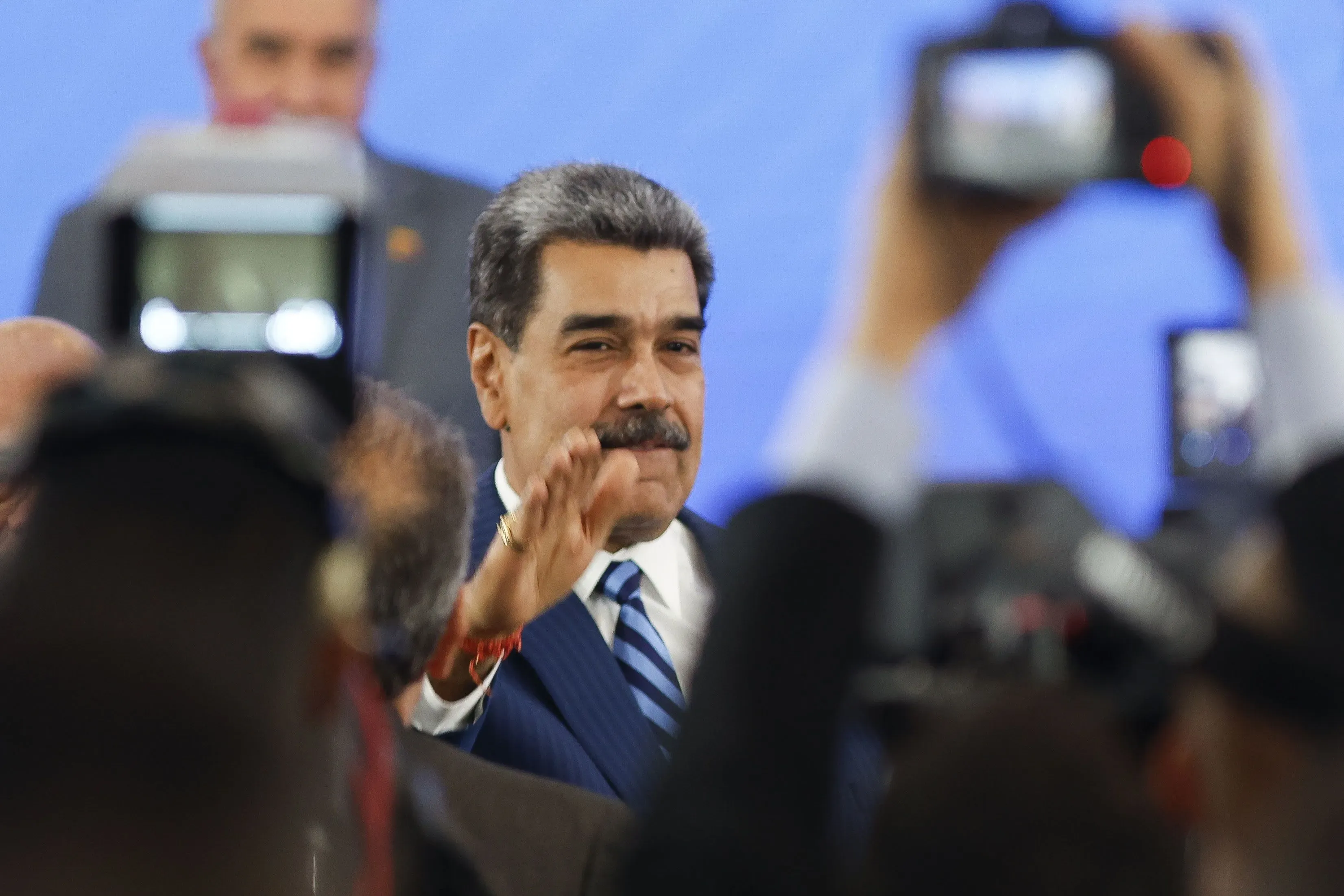 نيكولاس مادورو، رئيس فنزويلا، يلوح للحضور وسط مجموعة من الكاميرات، مما يعكس التوترات السياسية الحالية في البلاد.