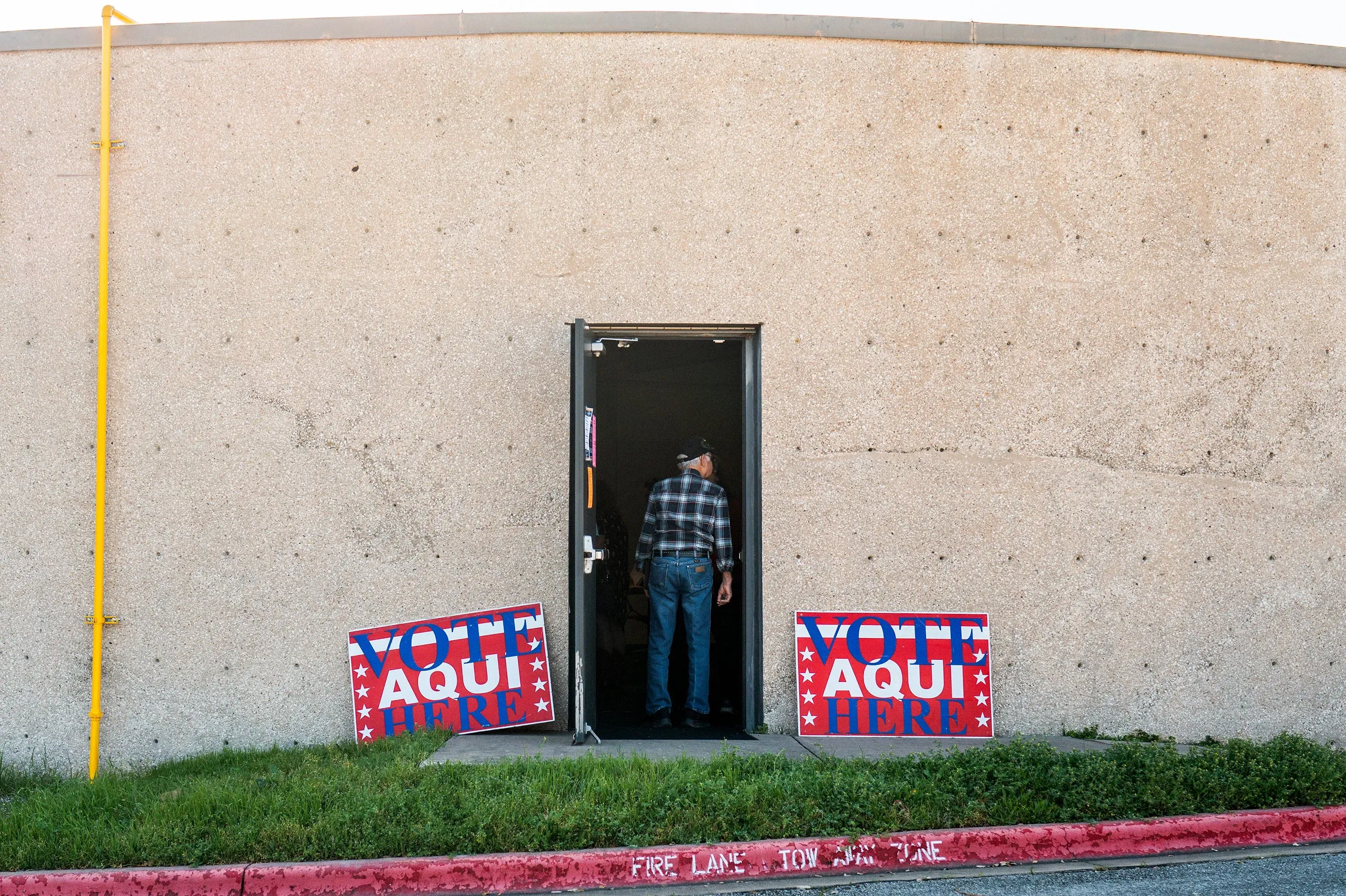 رجل يدخل مركز الاقتراع مع لافتات تشير إلى "صوت هنا" باللغتين الإنجليزية والإسبانية، مما يعكس تزايد المشاركة اللاتينية في الانتخابات.