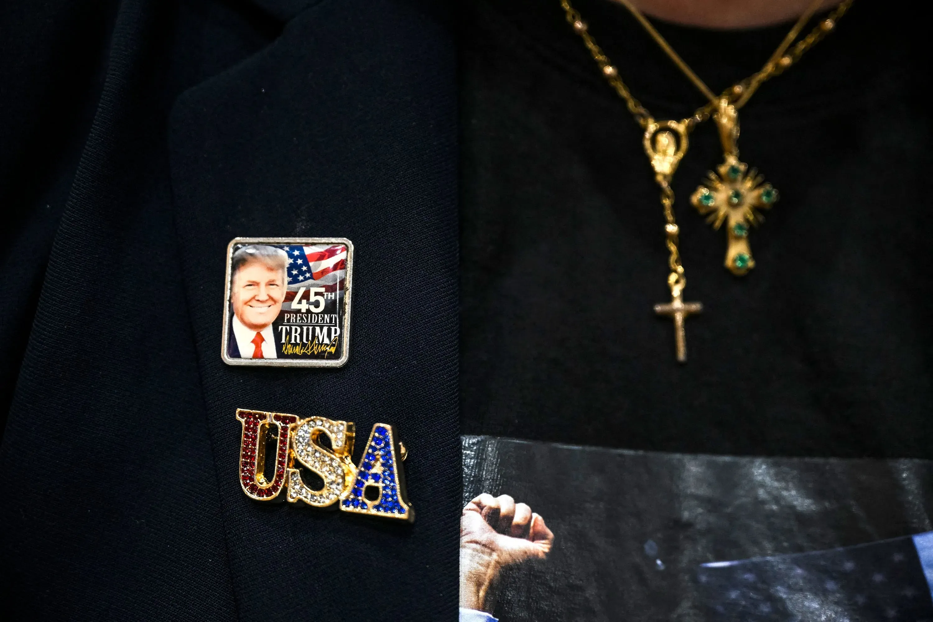 شعار يحمل صورة ترامب مع علم أمريكي، بالإضافة إلى قلائد صليبية، يعكس دعم بعض الناخبين اللاتينيين للرئيس السابق.