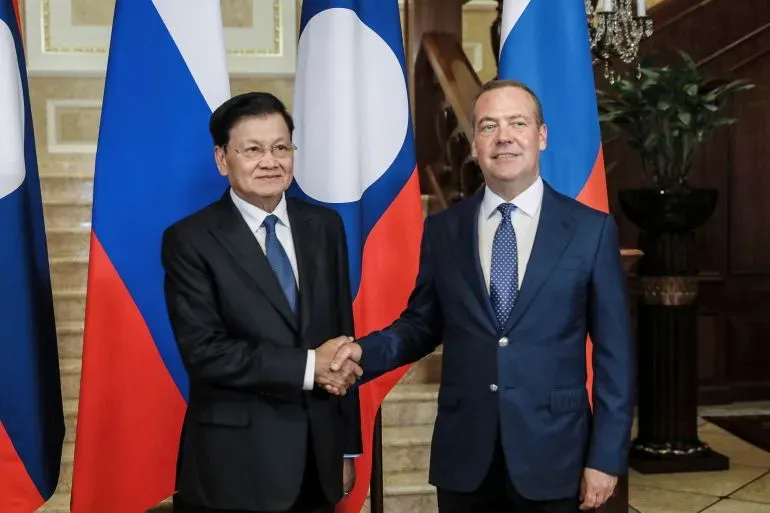 اجتماع بين ديمتري ميدفيديف ورئيس لاوس، مع العلميات الوطنية للبلدين خلفهما، يعكس التوترات الجيوسياسية الحالية.