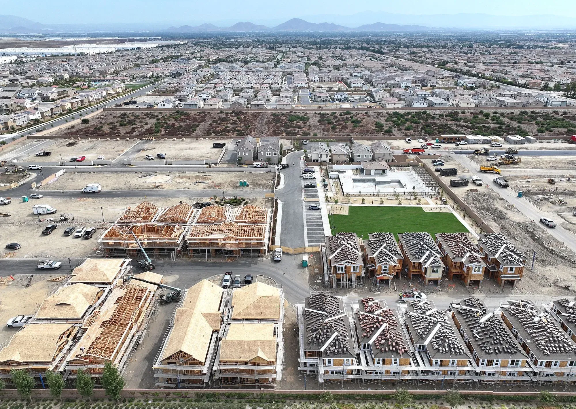 مشهد جوي لموقع بناء منازل جديدة مع منازل جاهزة في الخلفية، يوضح نشاط سوق الإسكان في الولايات المتحدة.