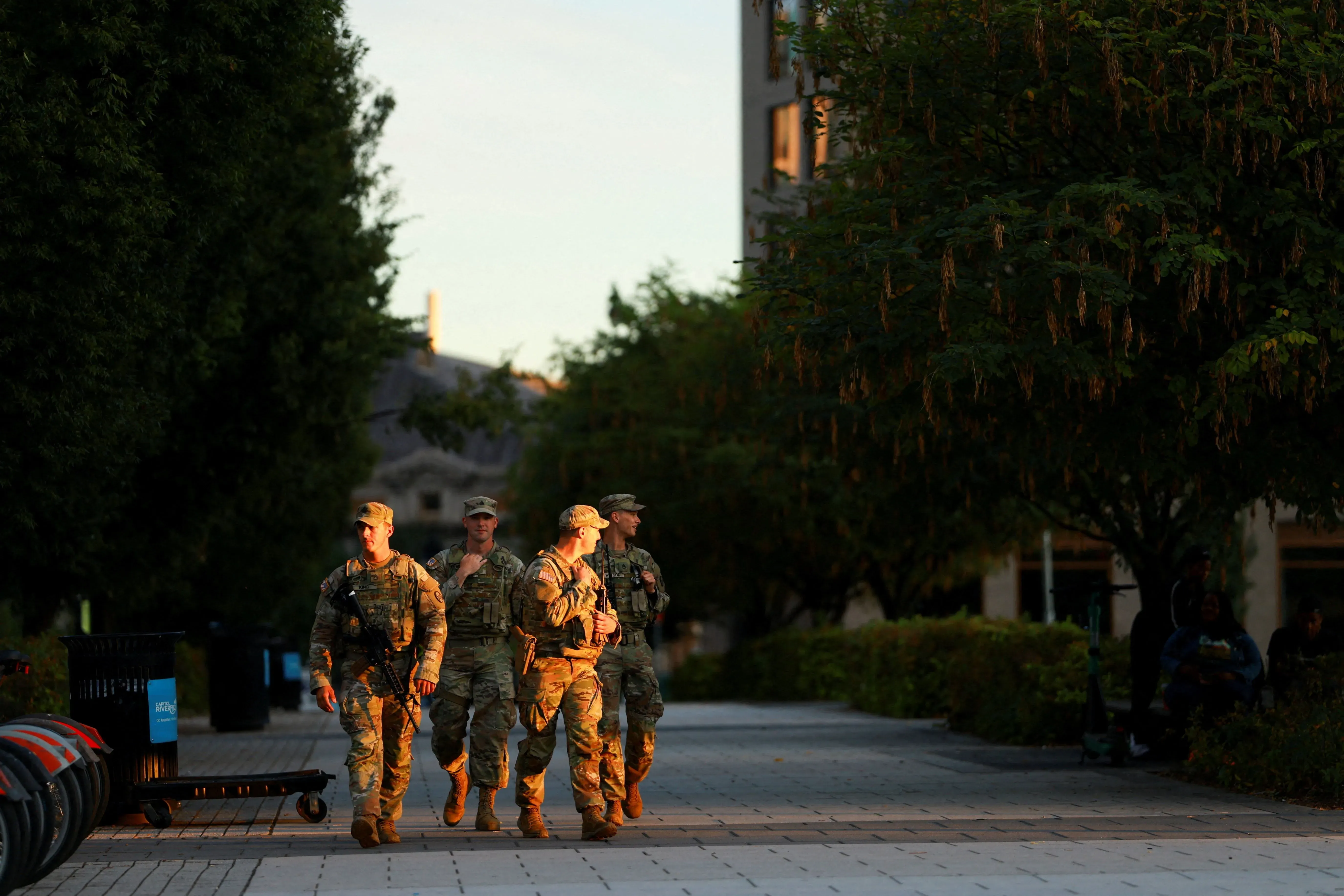 جنود يرتدون زيًا عسكريًا يتجولون في منطقة حضرية، محاطين بأشجار خضراء، في سياق من التوترات السياسية والقرارات الحكومية.