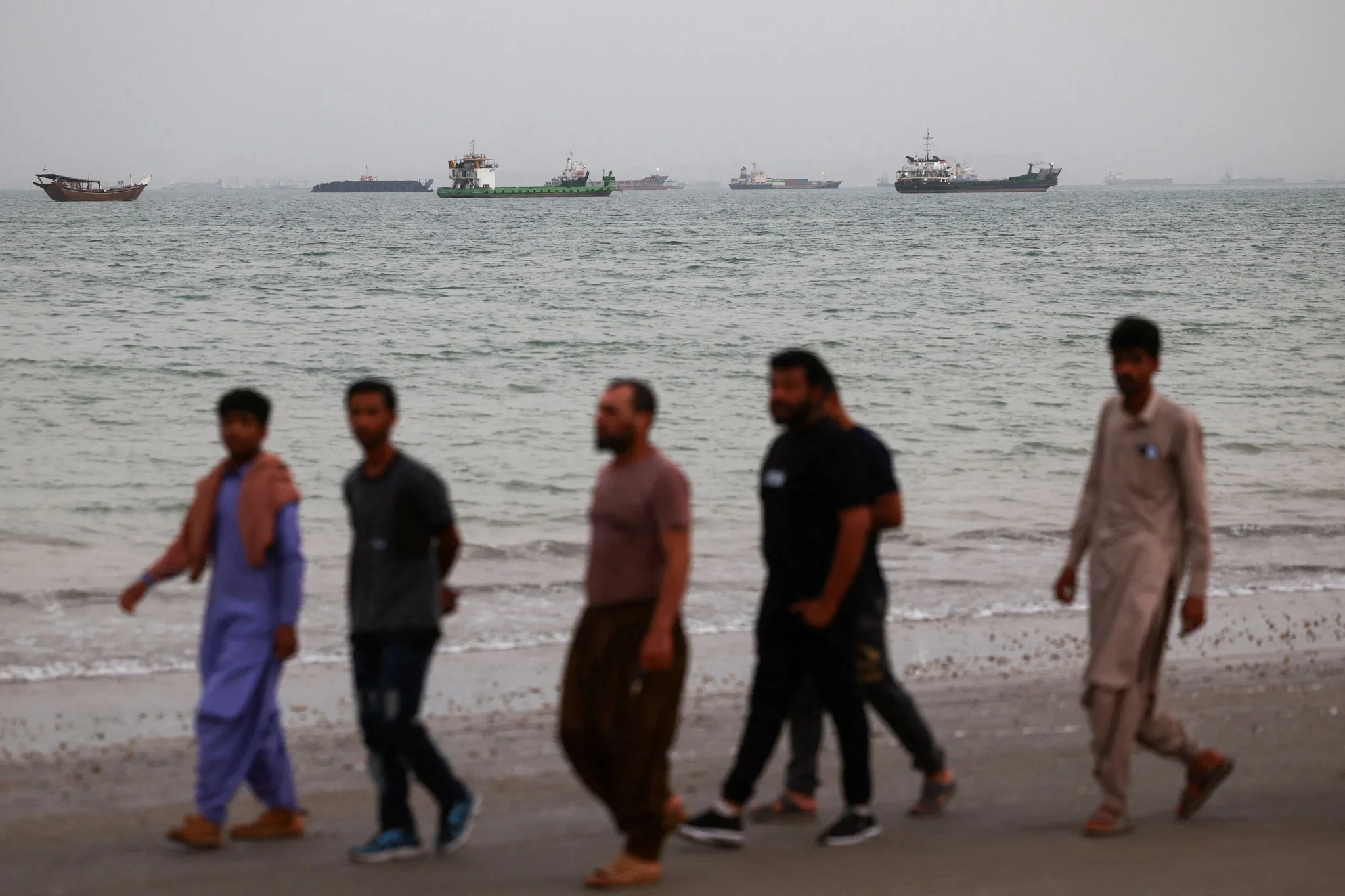 مجموعة من الأشخاص يمشون على شاطئ، مع ظهور سفن في البحر، في سياق المفاوضات بين إيران والولايات المتحدة حول إنهاء الحرب.