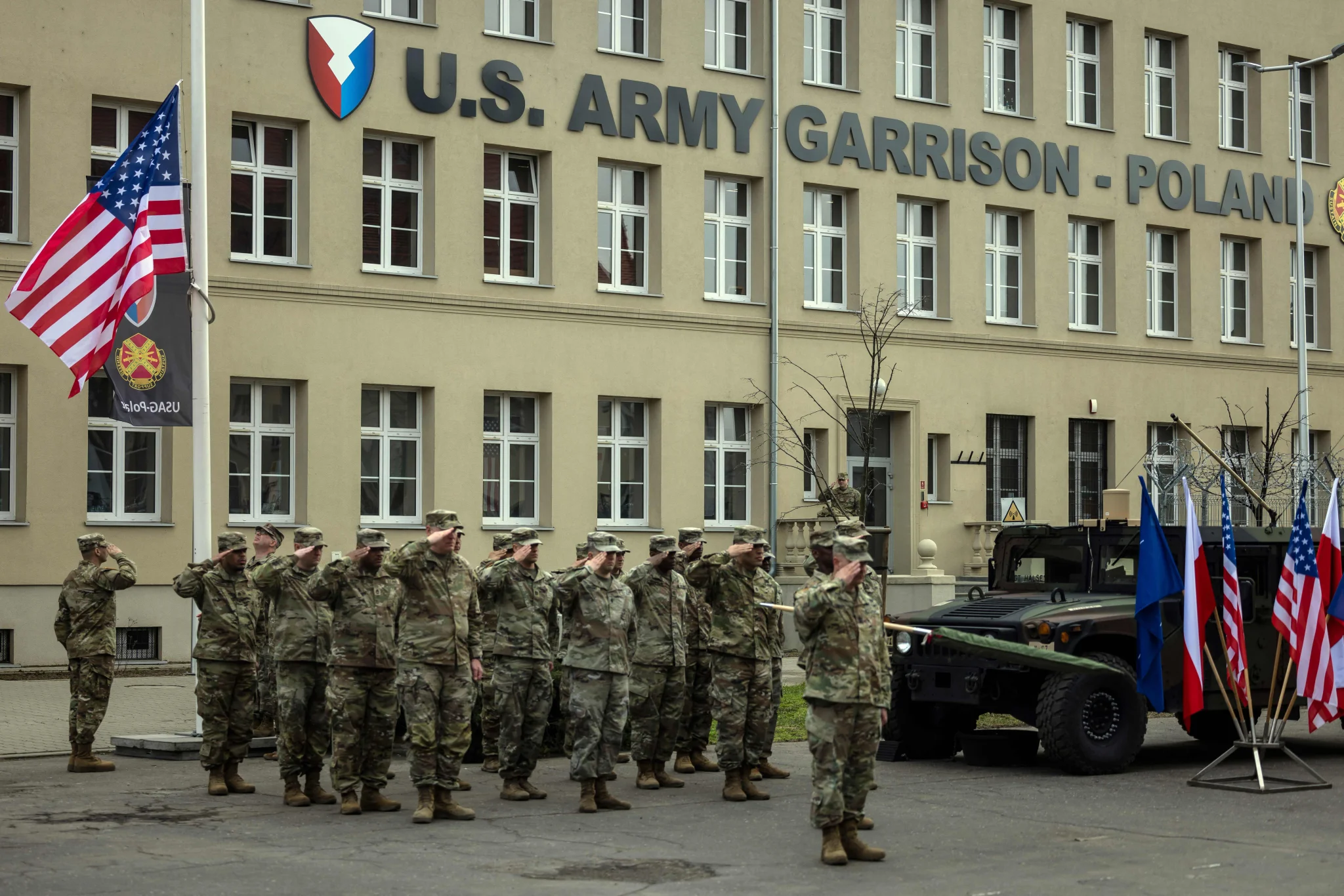 جنود أمريكيون يؤدون التحية أمام قاعدة "US Army Garrison Poland"، مع أعلام الولايات المتحدة وبولندا، في سياق تعزيز الوجود العسكري الأمريكي في أوروبا.