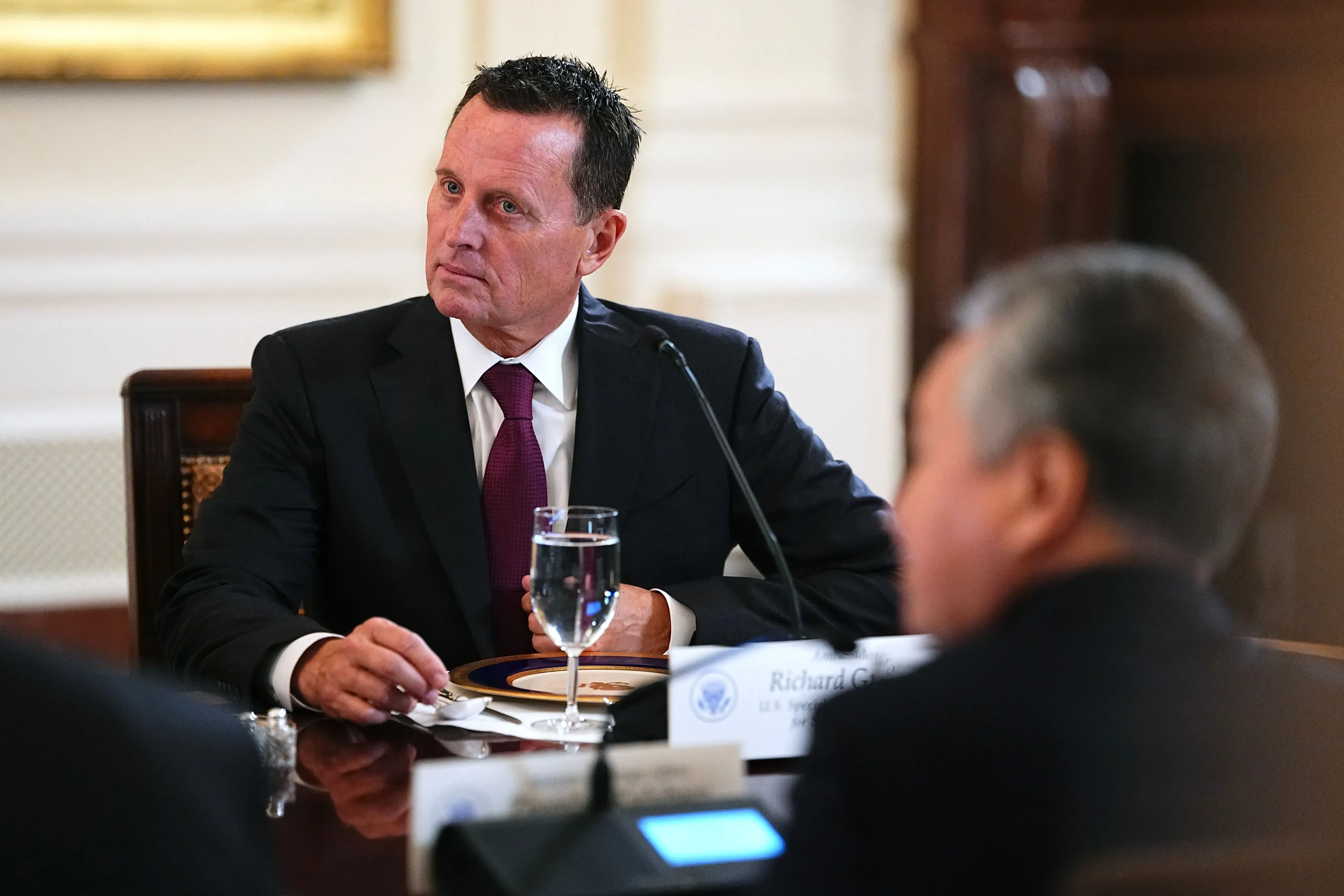 ريتشارد غرينيل، الرئيس السابق لمركز كينيدي، يجلس في اجتماع رسمي، مع نظرة تأملية، وسط أجواء من التوتر والضغط.