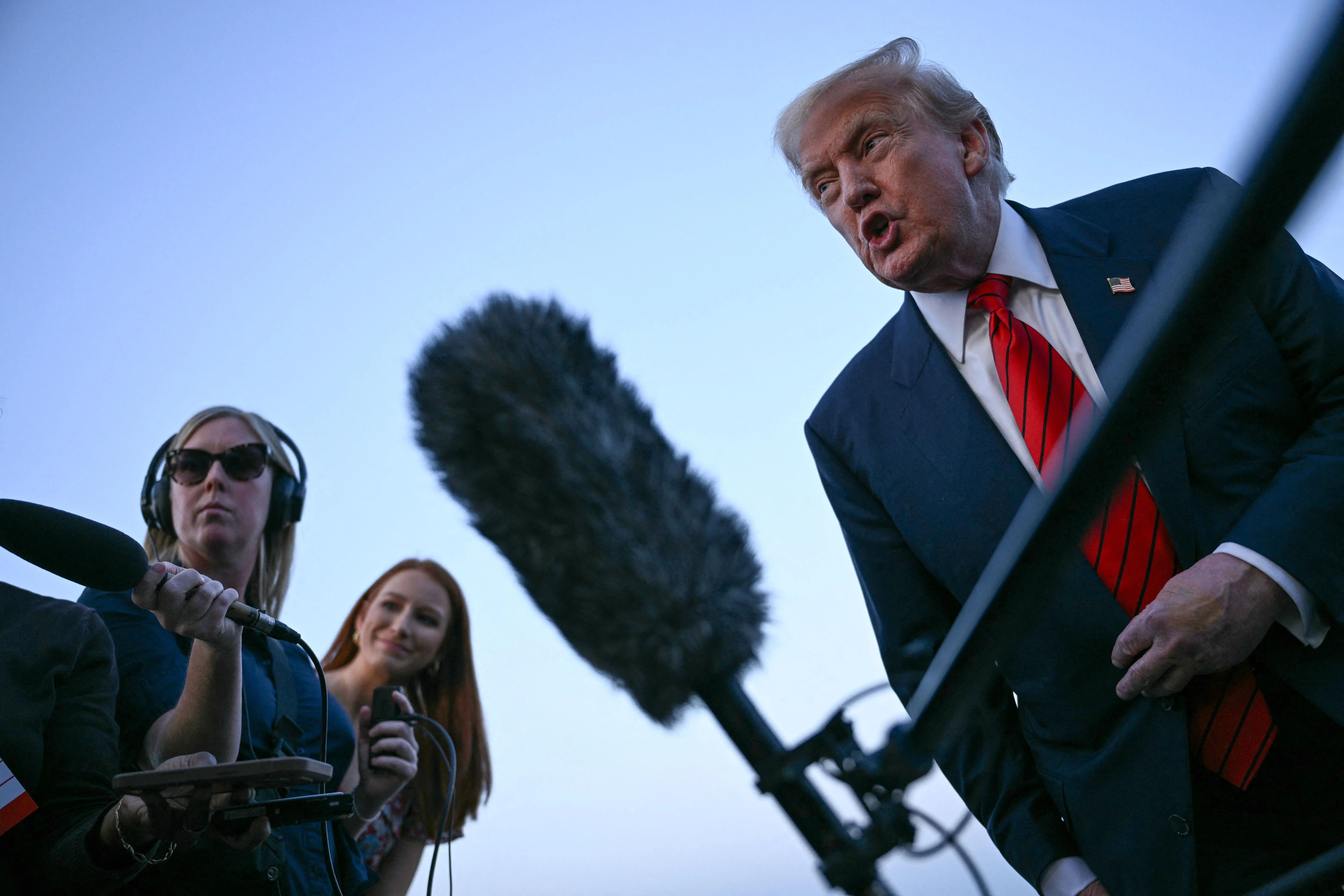 ترامب يتحدث بحماس أثناء مؤتمر صحفي، مع وجود صحفيتين خلفه. تعكس تعابير وجهه استياءه من تقارير الوظائف الأخيرة.