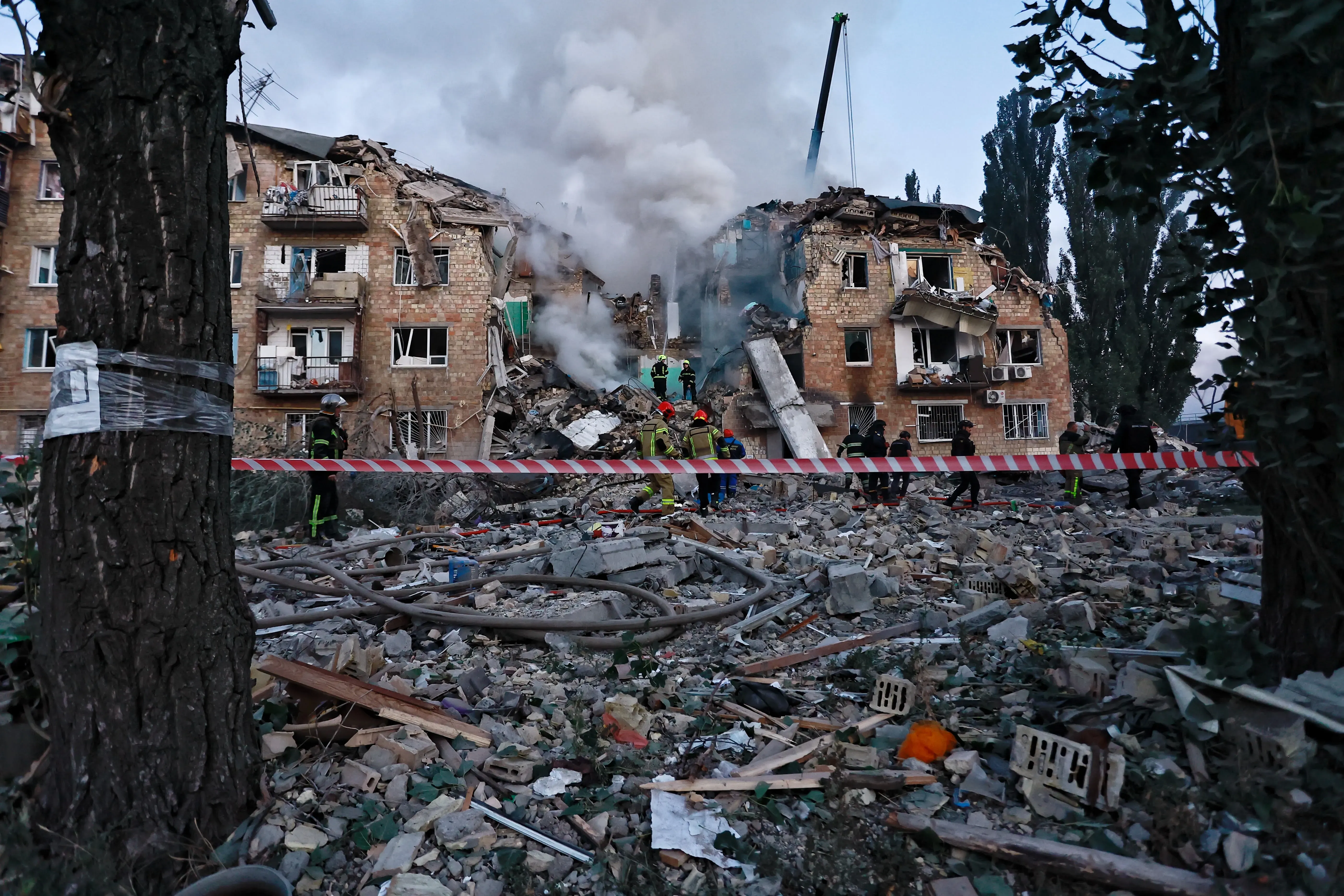 دخان يتصاعد من مبنى مدمر في أوكرانيا، حيث يقوم رجال الإنقاذ بعمليات البحث وسط الأنقاض، مما يعكس آثار العدوان الروسي.