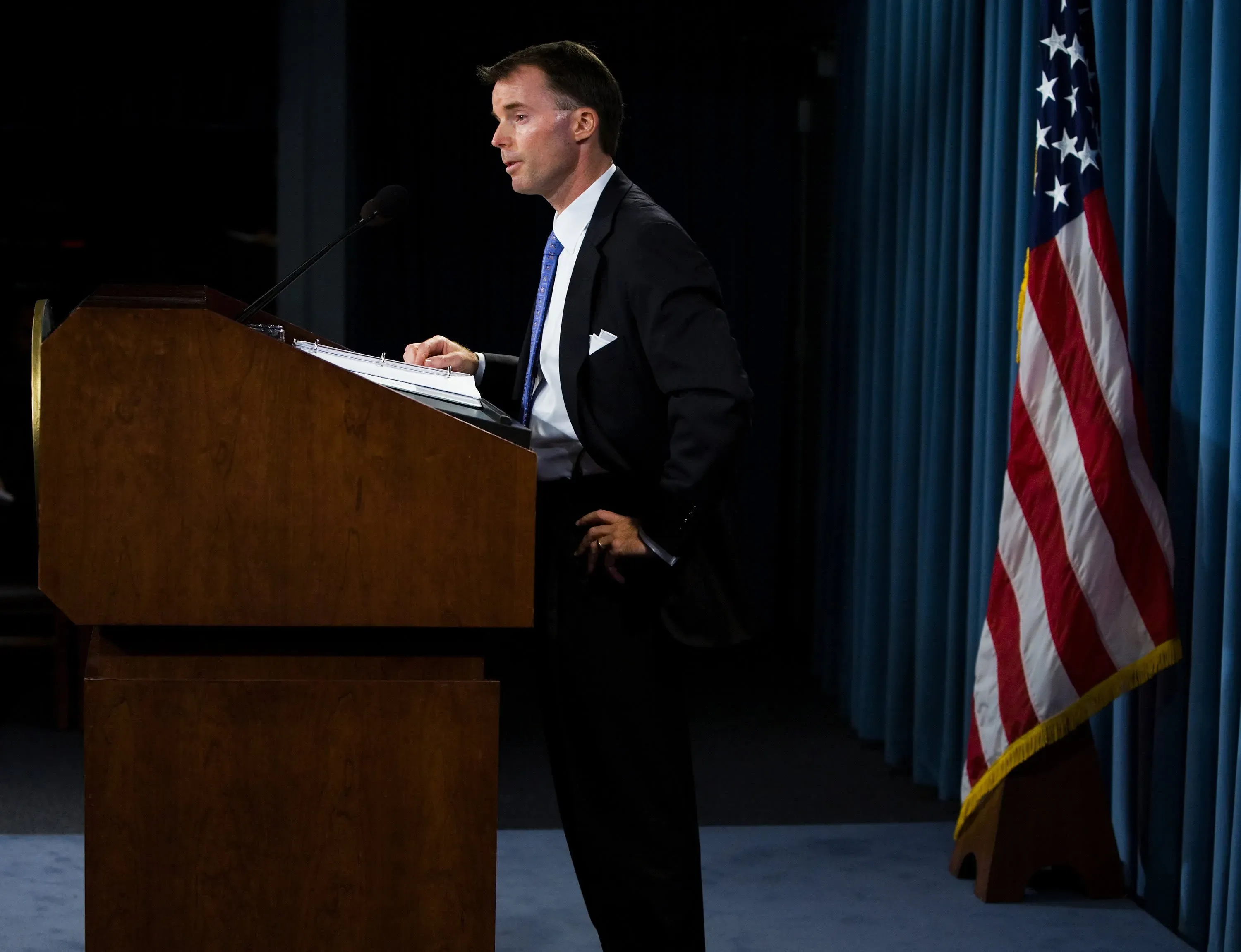 رجل يرتدي بدلة رسمية يتحدث من منصة أمام ستار أزرق، مع وجود علم أمريكي خلفه، في مؤتمر صحفي حول قانون RICO.