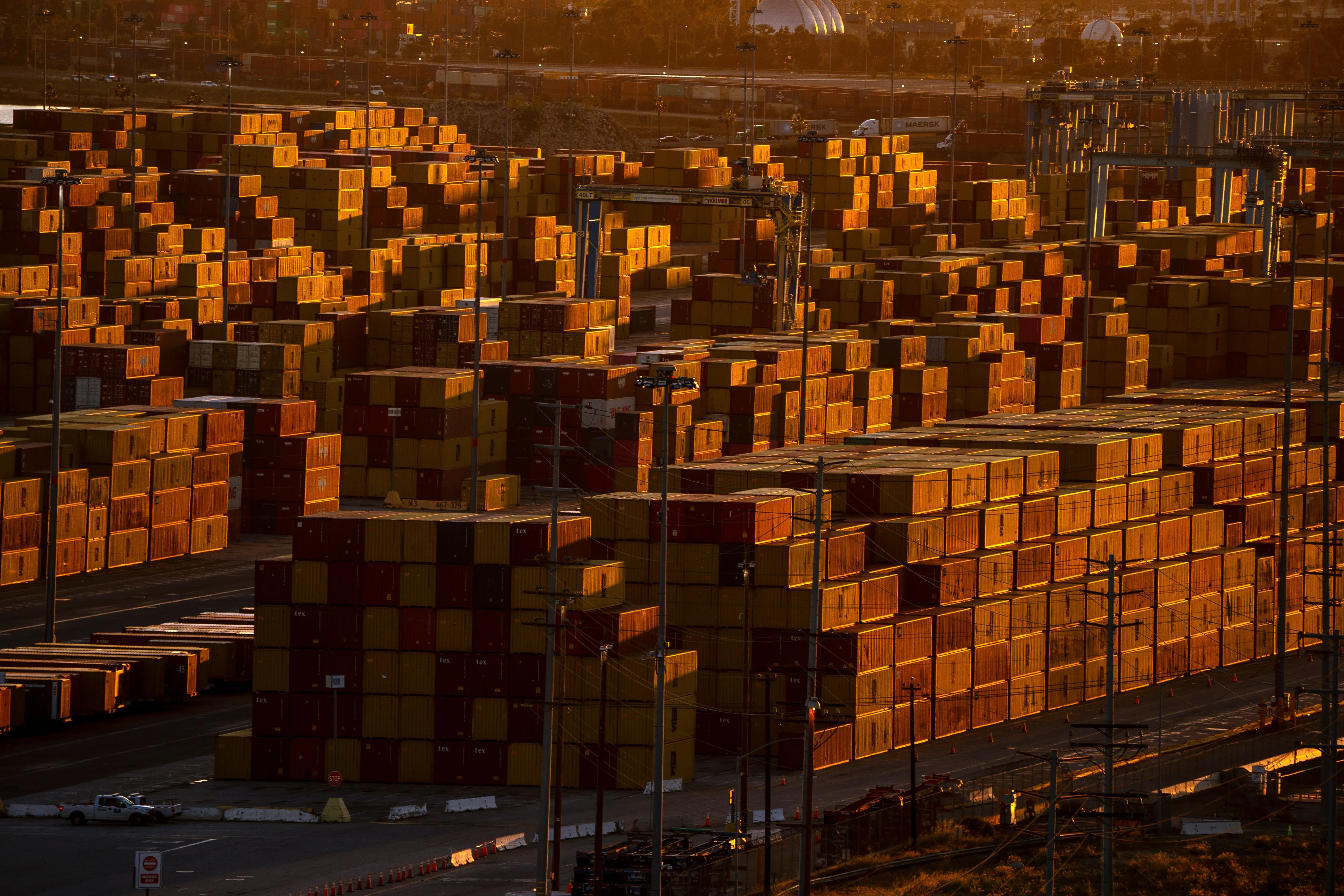 صورة لمستودع يحتوي على حاويات شحن ملونة، تعكس ضوء الشمس، مما يبرز حجم التجارة وتأثير التعريفات الجمركية على الاقتصاد.