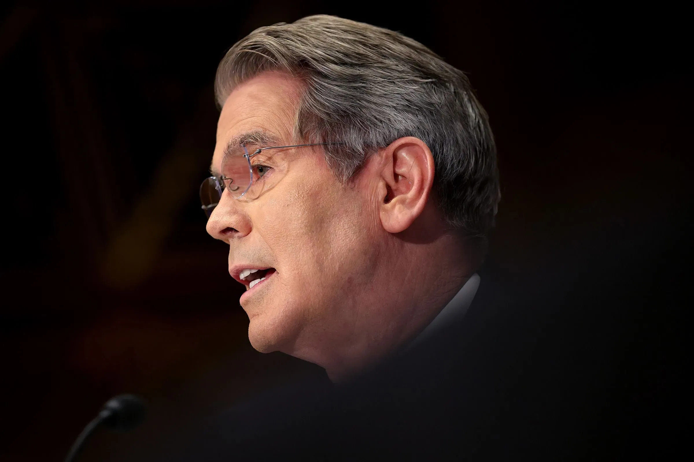 رجل يتحدث في جلسة استماع، مع التركيز على وجهه وتعبيرات وجهه، بينما يظهر جزء من خلفية غير واضحة.