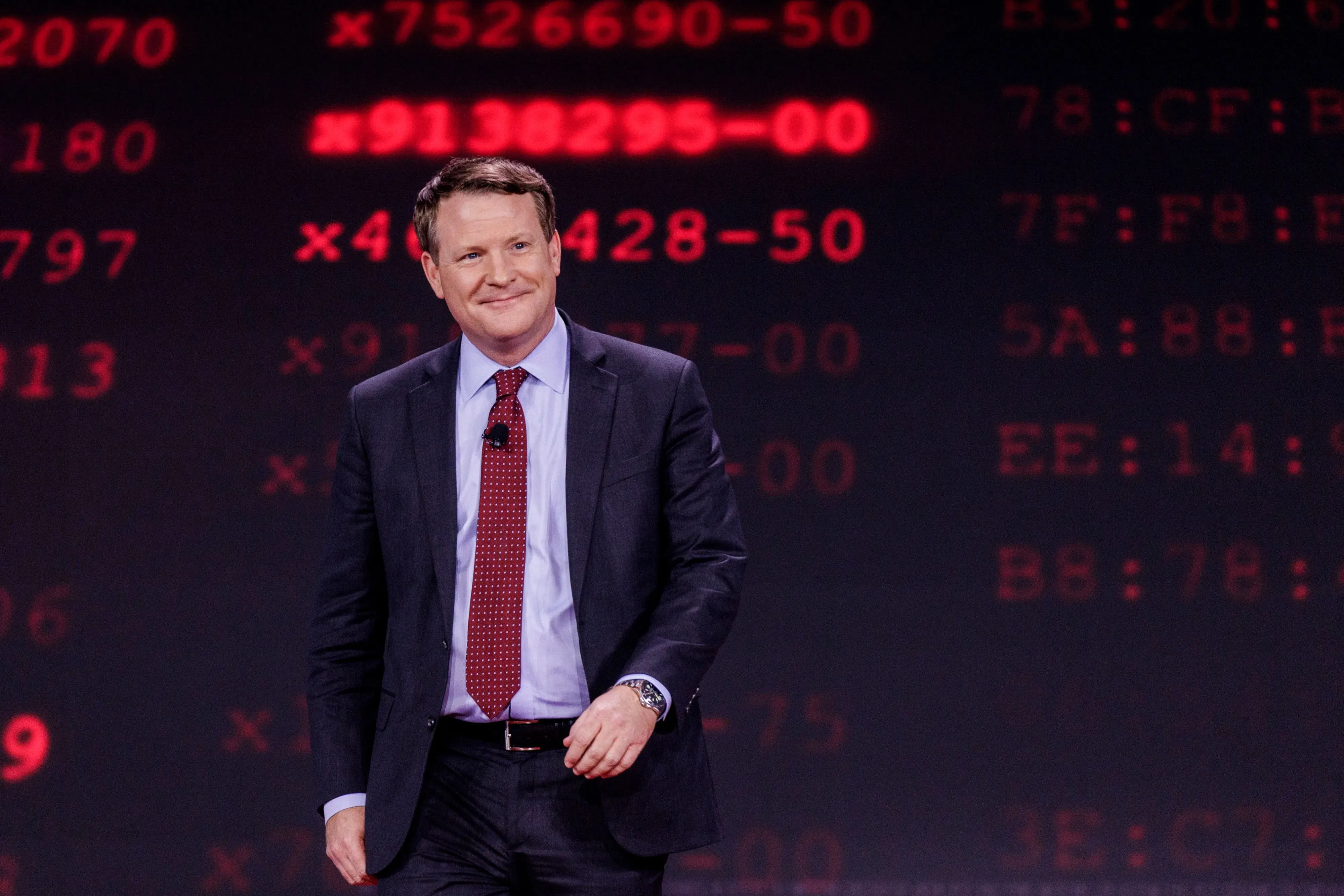 ديفيد ساكس، مسؤول الذكاء الاصطناعي في البيت الأبيض، يتحدث على المسرح أمام خلفية رقمية حمراء، أثناء مناقشة مستقبل الذكاء الاصطناعي.