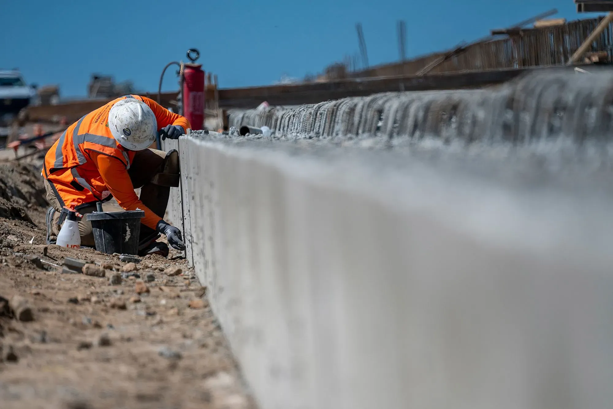 عامل يرتدي سترة واقية وقبعة، يعمل على بناء جدار خرساني في موقع إنشائي، مما يعكس جهود التوظيف في قطاع البناء.