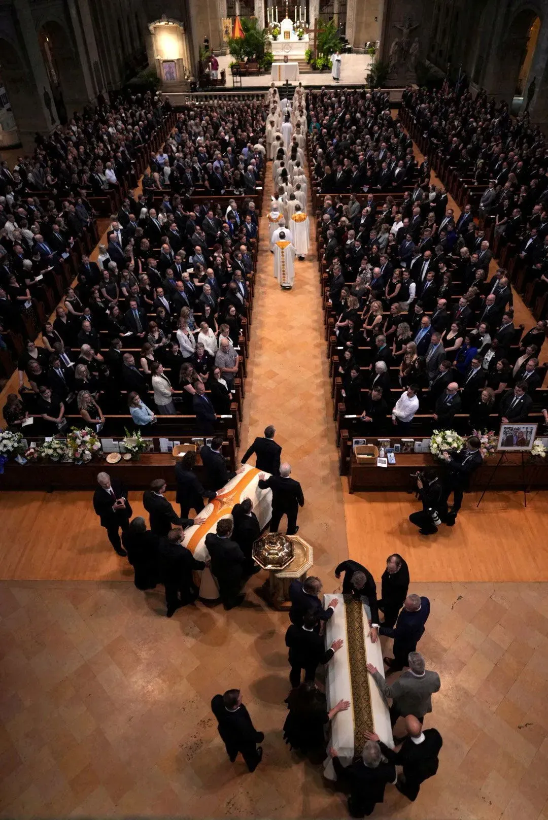 تجمع حشود كبيرة في كنيسة خلال مراسم تأبين، حيث يُحمل النعش وسط أجواء حزينة، مع وجود رجال دين في المقدمة.