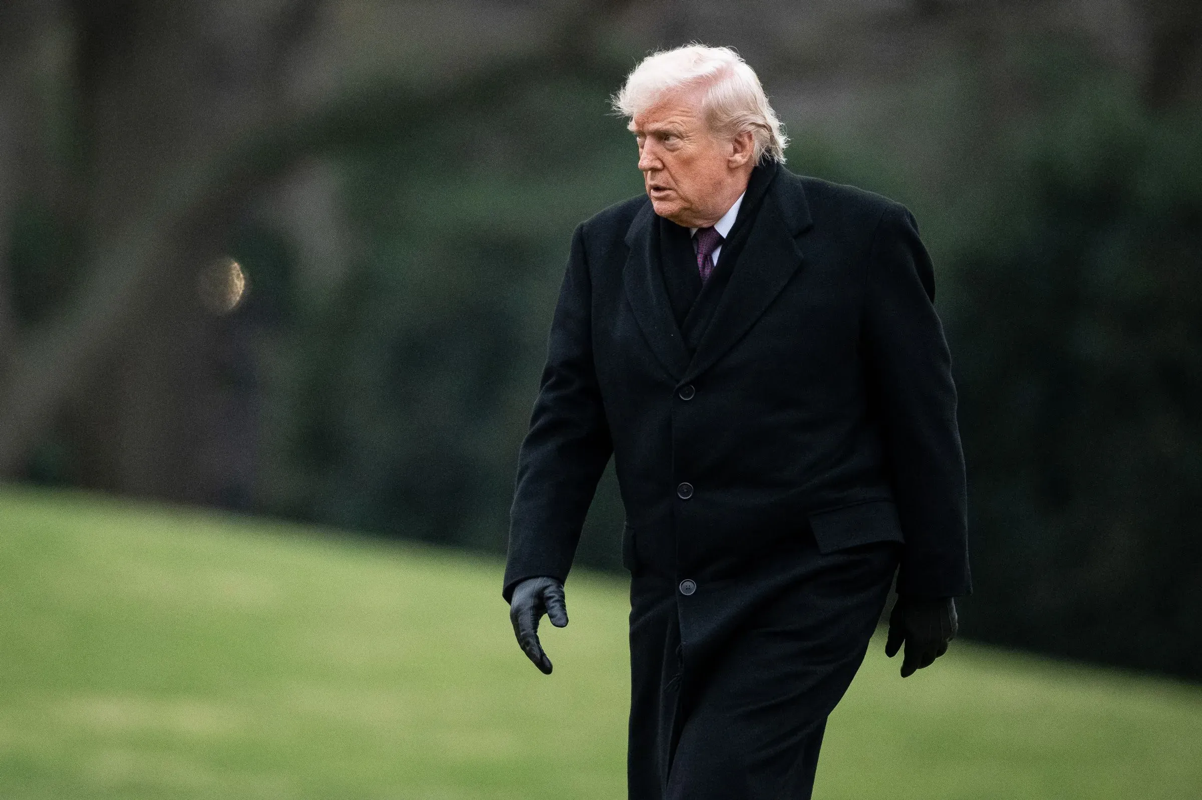 دونالد ترامب يسير في حديقة البيت الأبيض مرتديًا معطفًا أسود وقفازات، مع تعبير وجه يعكس الجدية في ظل تراجع شعبيته.